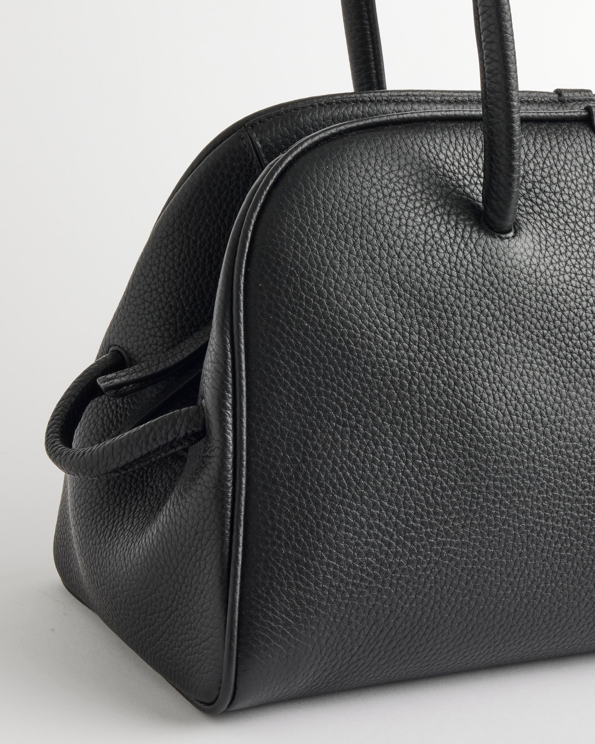 A close-up of the Jacquemus Le Turismo Bag, a black textured leather bowling bag with rounded edges and dual handles, displayed against a plain light background.