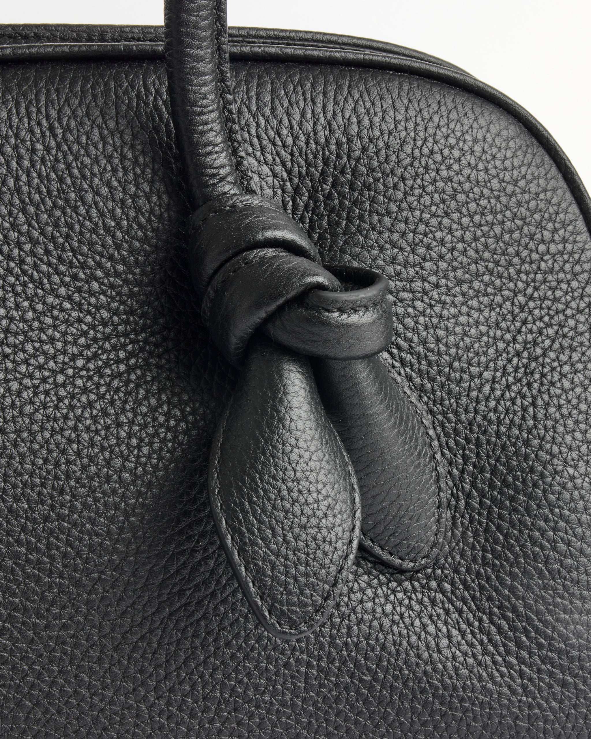 Close-up of the Jacquemus Le Turismo Bag, highlighting the knotted handle detail against its textured black leather surface.