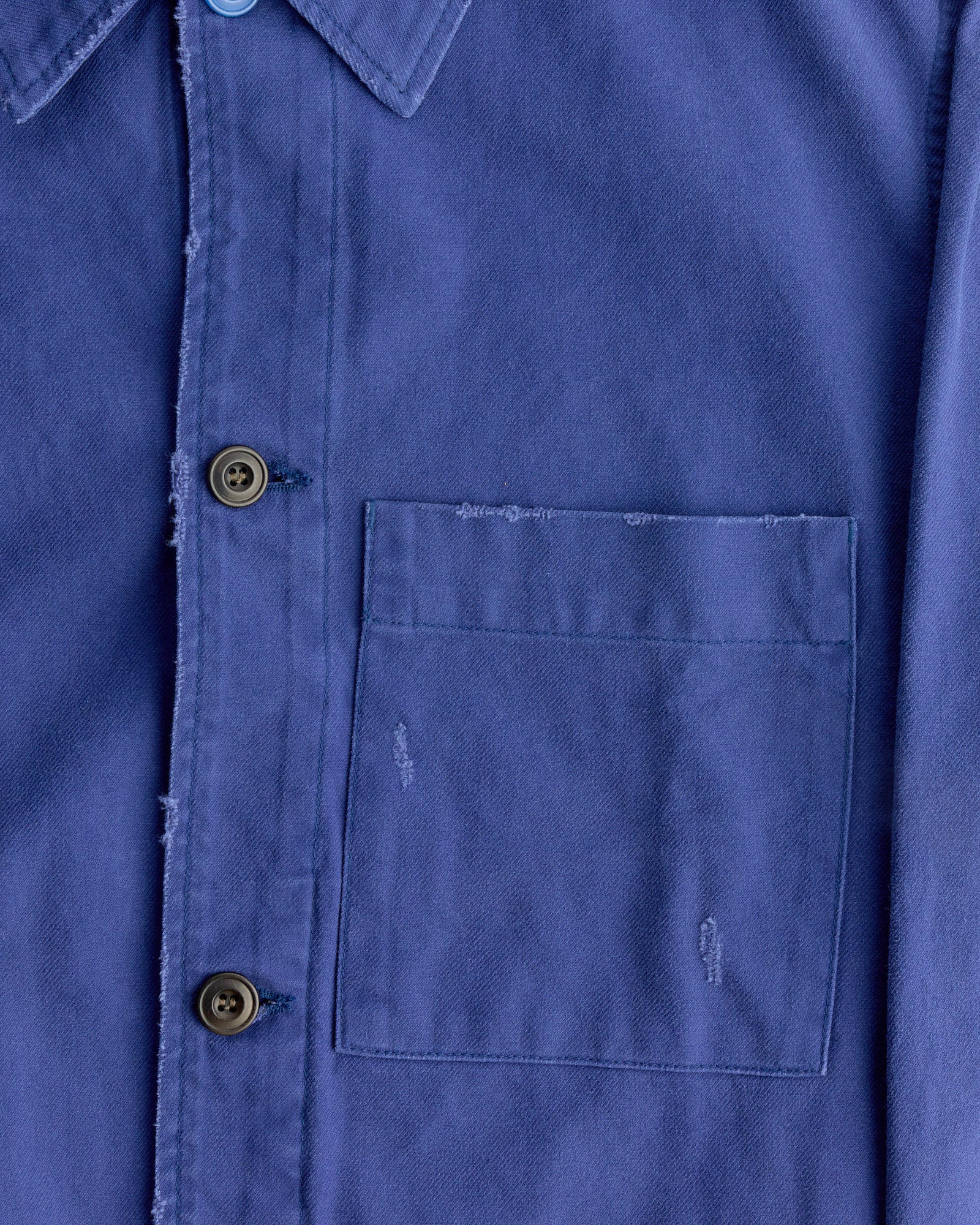 Close-up of the SMOCK Lang Jacket in French Cotton Twill Blue shows a chest pocket, two buttons, and subtle distressed details by the pocket and edges, crafted from Japanese-woven French cotton twill.