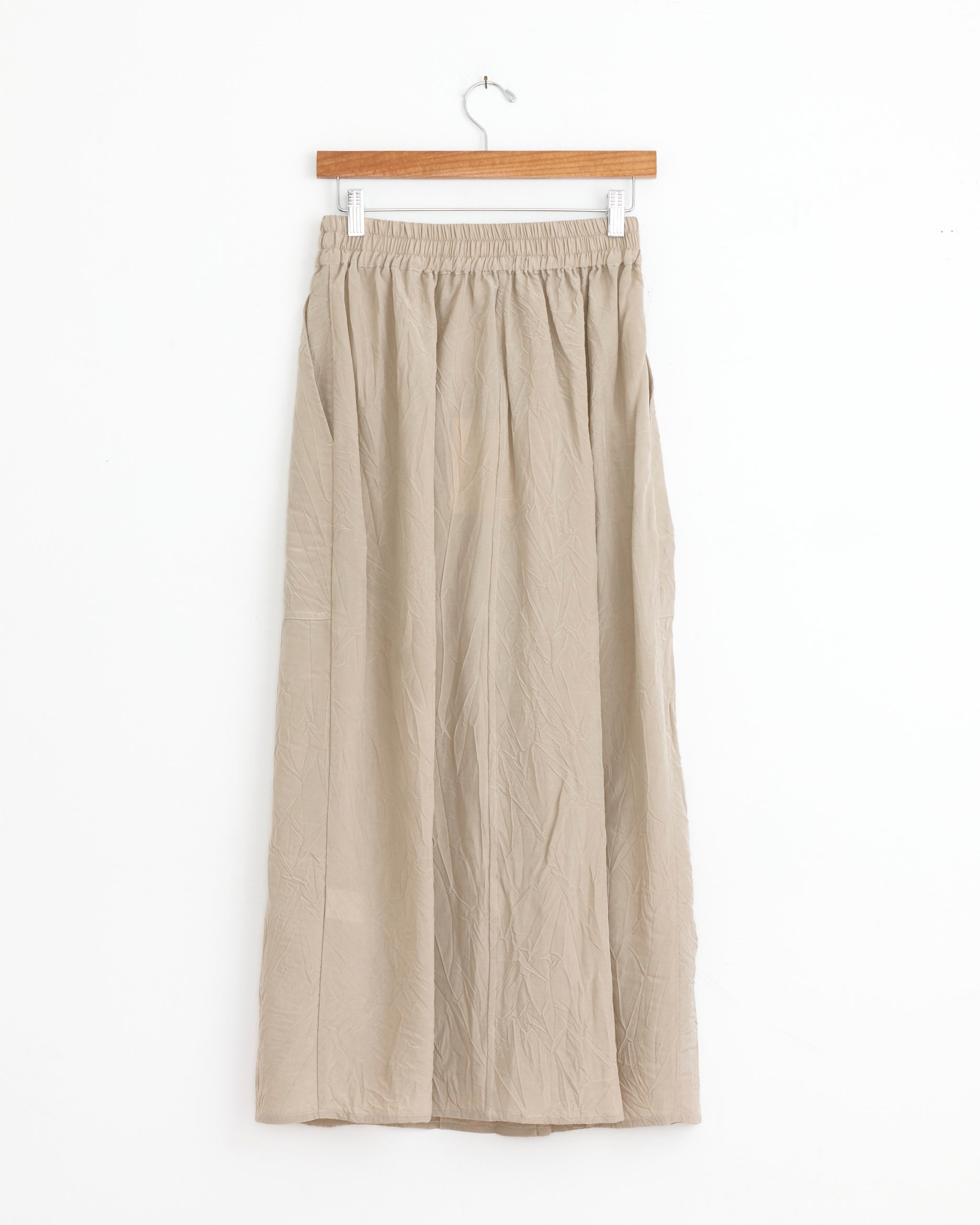 The Studio Nicholson Oates Skirt in Sable is an ankle-length skirt with Italian patch pockets, an elasticated waistband, and a flowy fit—subtle workwear influences for effortless style. Shown on a wooden hanger against a white background.