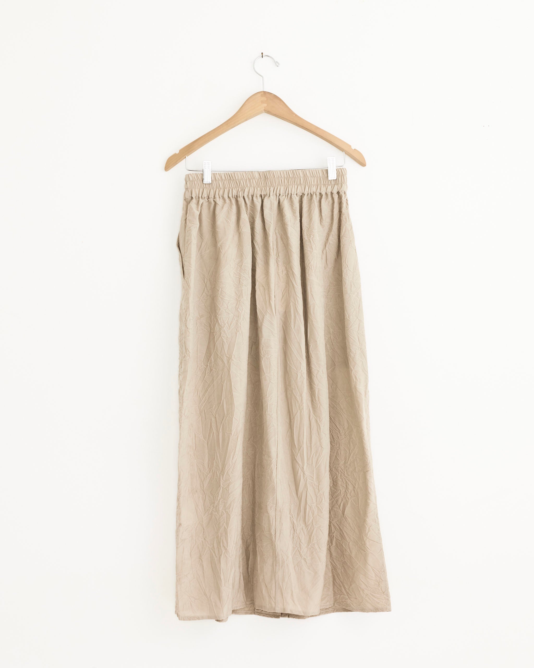 The Oates Skirt in Sable by Studio Nicholson, featuring Italian patch pockets and an elastic waistband, hangs on a wooden hanger against a plain white background.