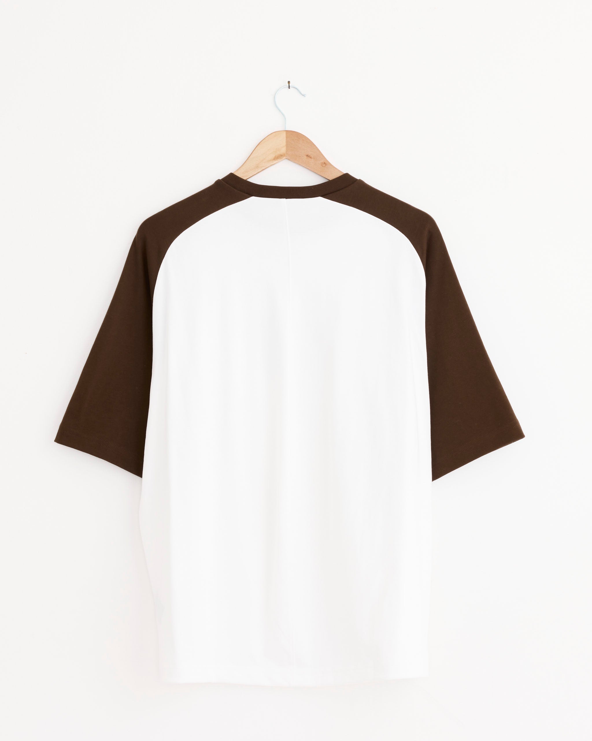 The Tibi Perfect Baseball T-Shirt in Brown Multi features a relaxed fit, 100% cotton, with a short white body and dark brown raglan sleeves, shown from the back on a hanger against a plain white background.