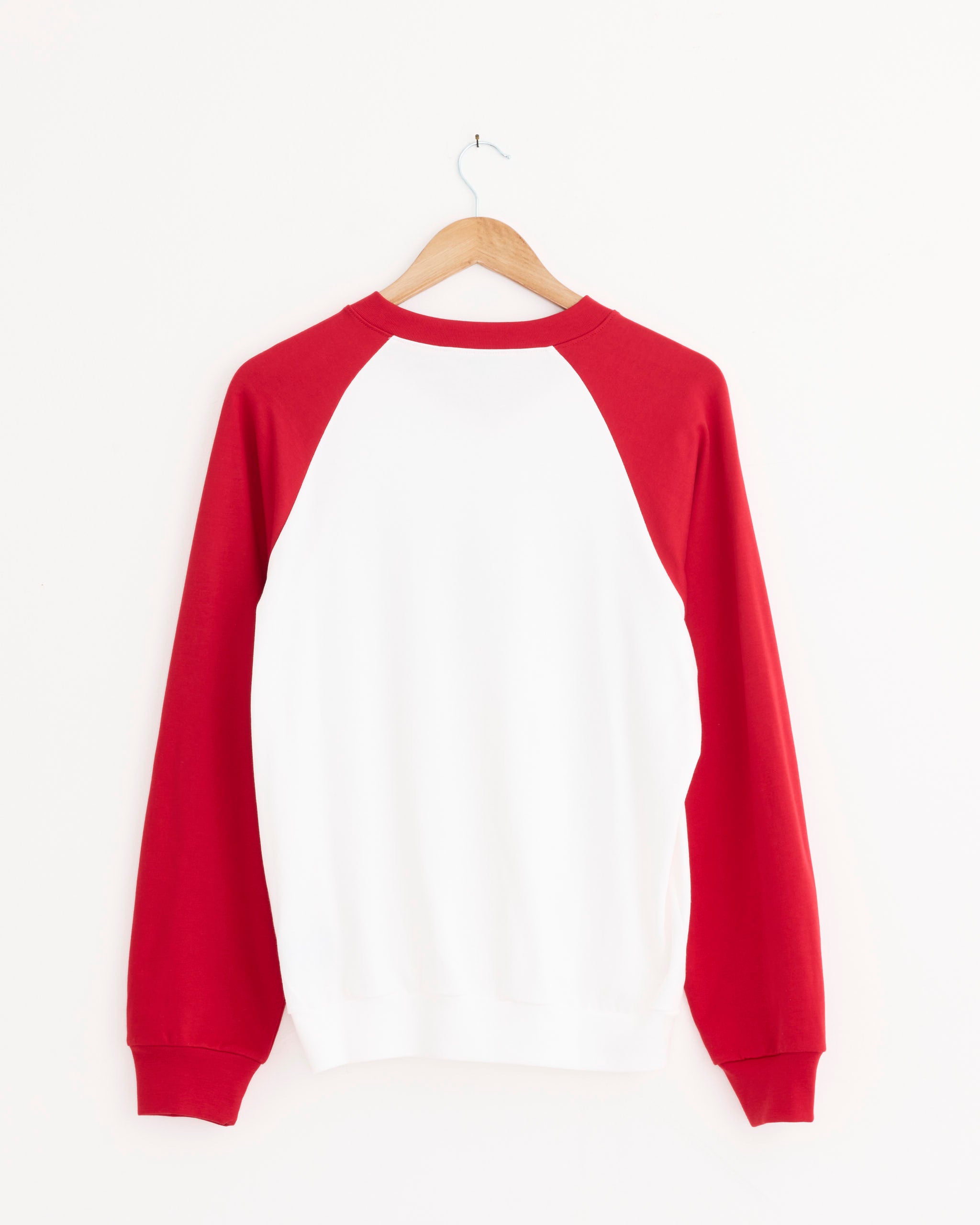 The Tibi Perfect Vintage Sweatshirt in Red Multi, featuring long red raglan sleeves, hangs on a wooden hanger against a white wall—a classic addition to your athletic wear collection.