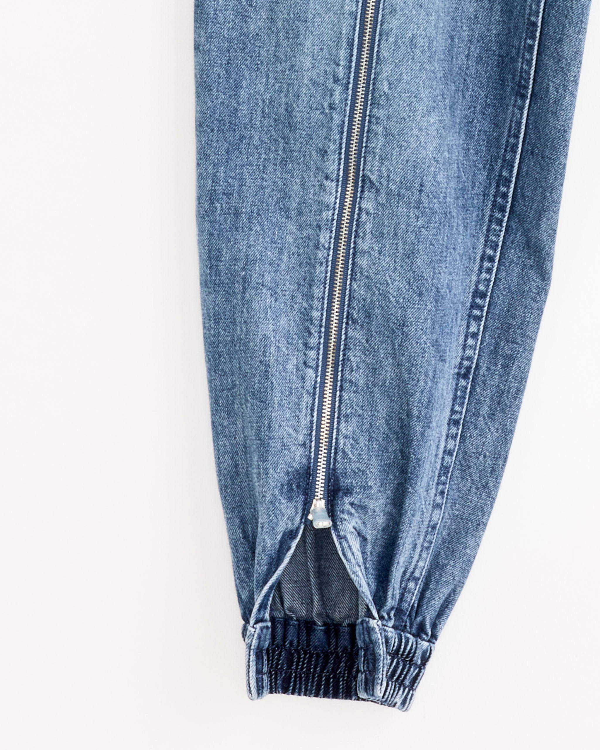Close-up of Tibi’s Zippered Denim Jogger in Classic Blue, showcasing an elastic cuff and vertical silver zipper along the ankle for a modern jogger look.