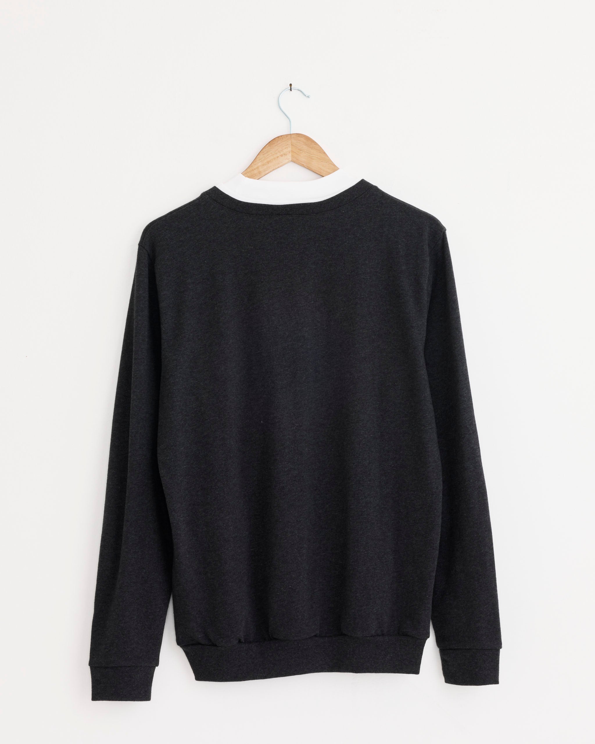 The Tibi Perfect Trompe Loeil Top in Grey Multi, featuring a layered neckline and long sleeves, is displayed from the back on a wooden hanger against a white wall.