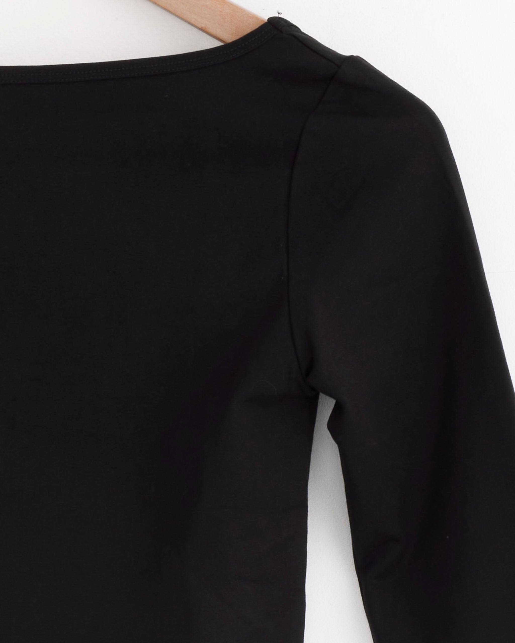 A close-up of the ST. AGNI Ballerina Top in Jet Black hangs on a wooden hanger, highlighting the shoulder, sleeve, and neckline against a white background for a refined, minimalist look.