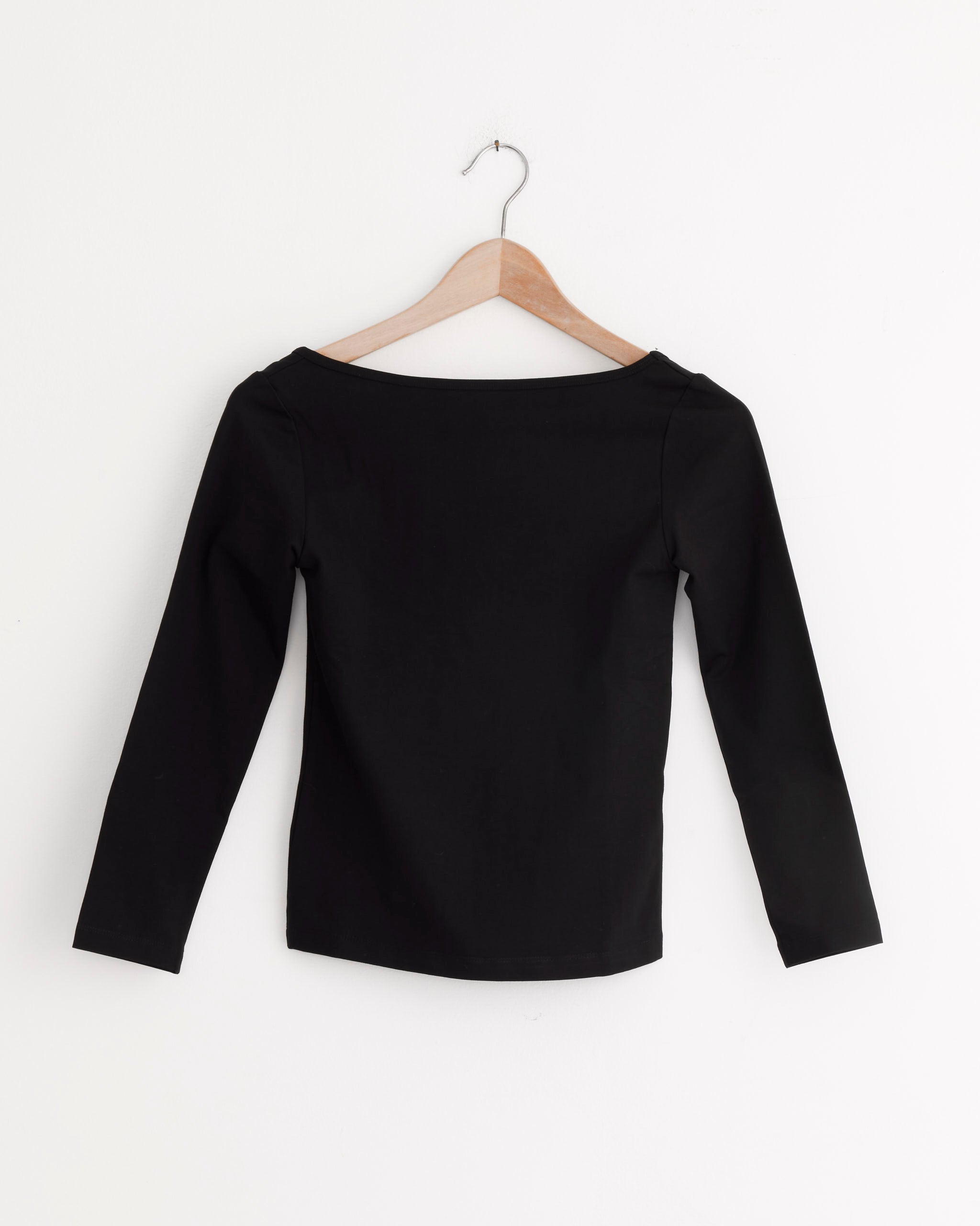 The ST. AGNI Ballerina Top in Jet Black, featuring a minimalist silhouette, is displayed from the back on a wooden hanger against a white wall.