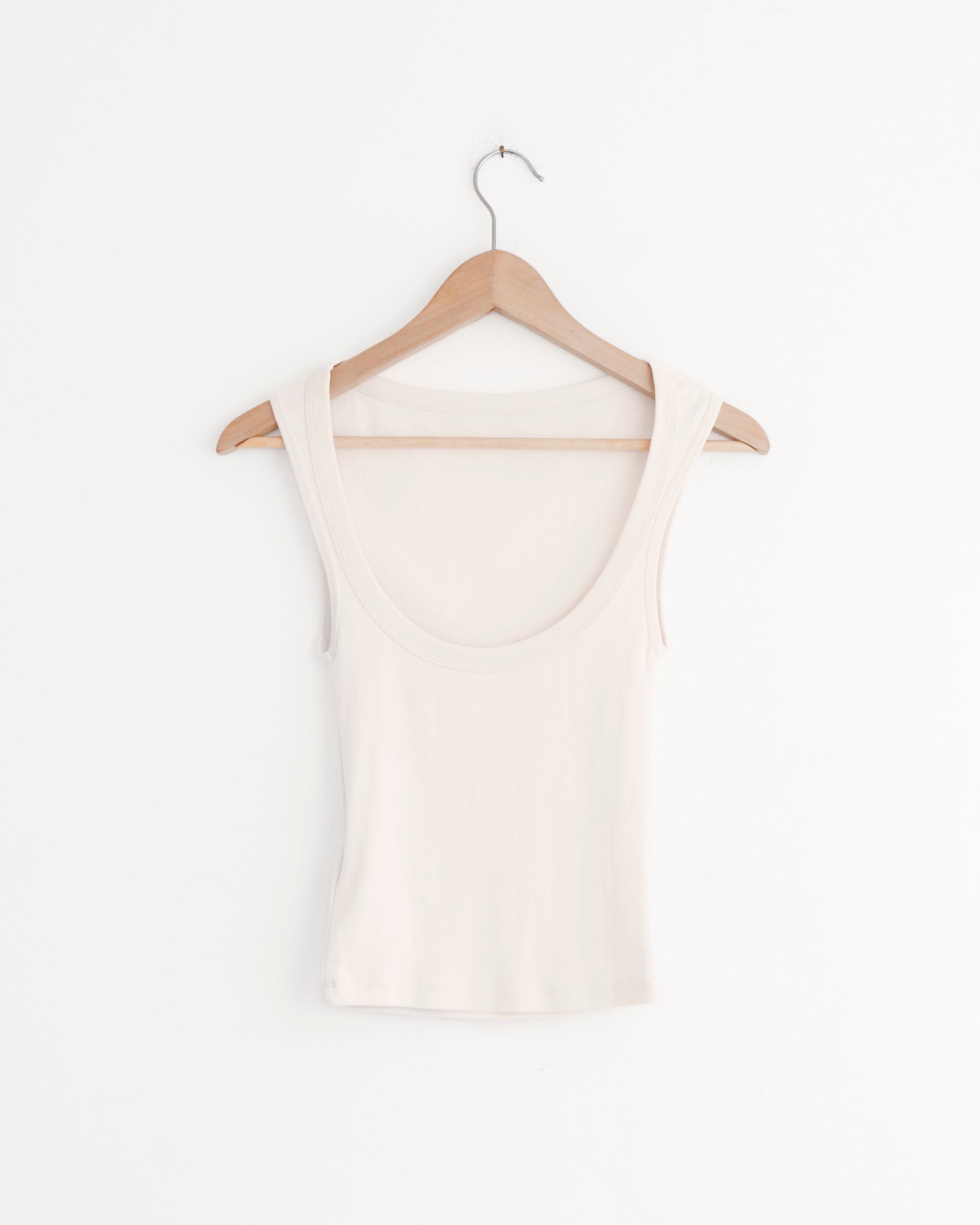 A sleeveless, scoop-neck Ballerina Top in Shell Pink by ST. AGNI made from organic cotton hangs on a wooden hanger against a plain white wall.