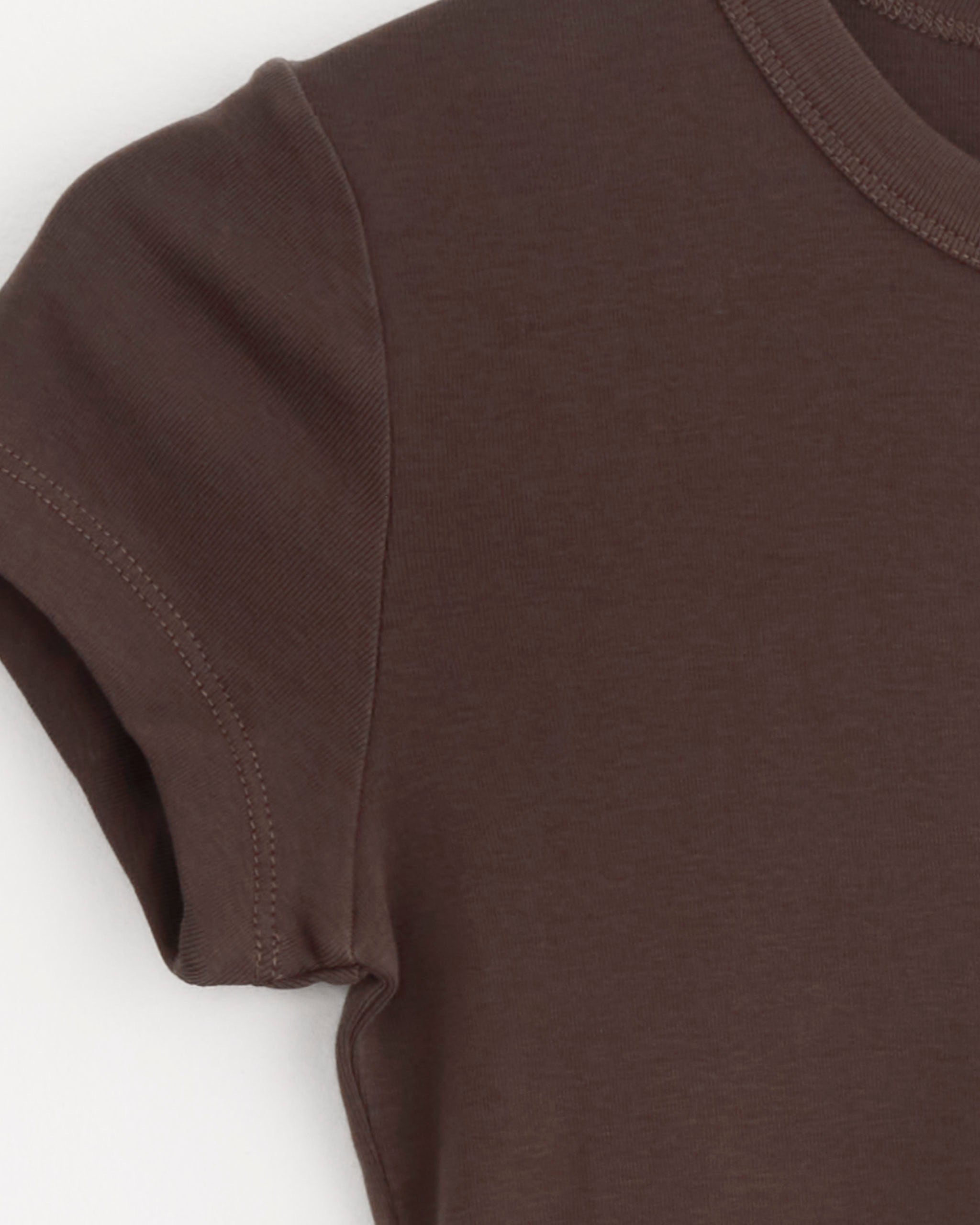 Close-up of the ST. AGNI Baby Tee in Fudge, highlighting the short sleeve, shoulder, and neckline with visible stitching details on soft brown organic cotton, set against a white background.