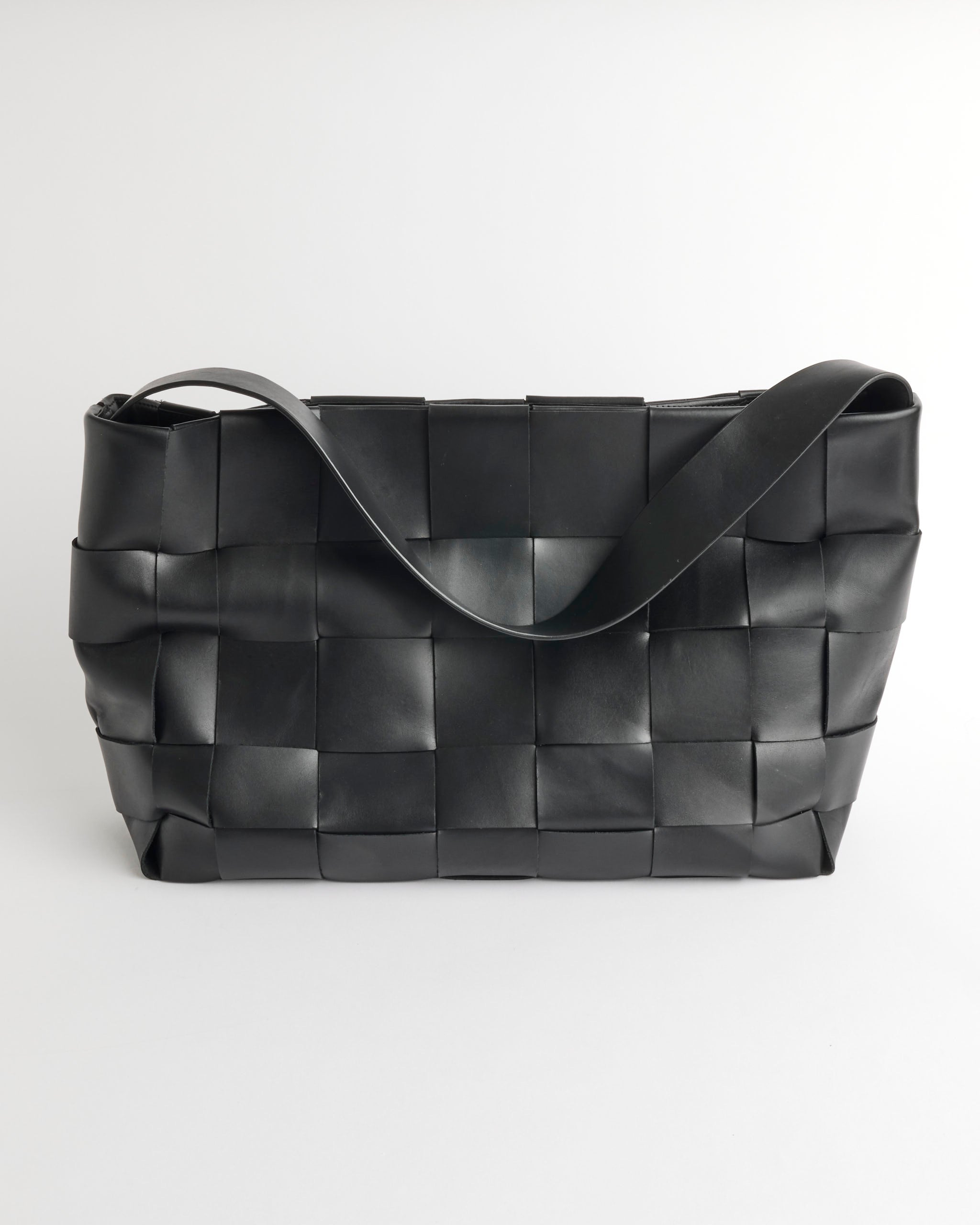 The ST. AGNI Woven Large Tote is a spacious black shoulder bag with wide woven leather strips and a single thick strap, shown on a plain white background.