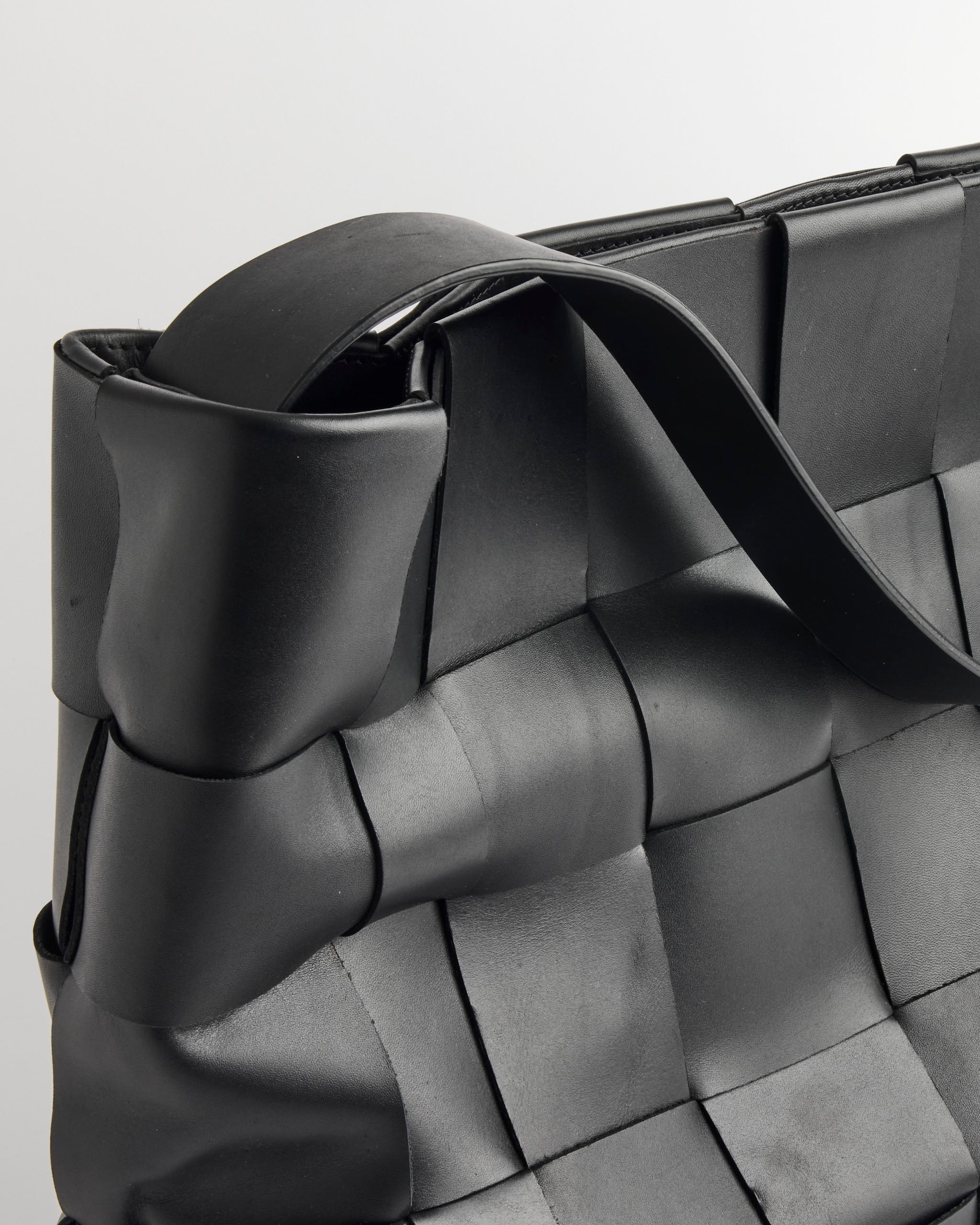 Close-up of the ST. AGNI Woven Large Tote, showcasing its black padded leather design and thick strap, set against a plain light background.