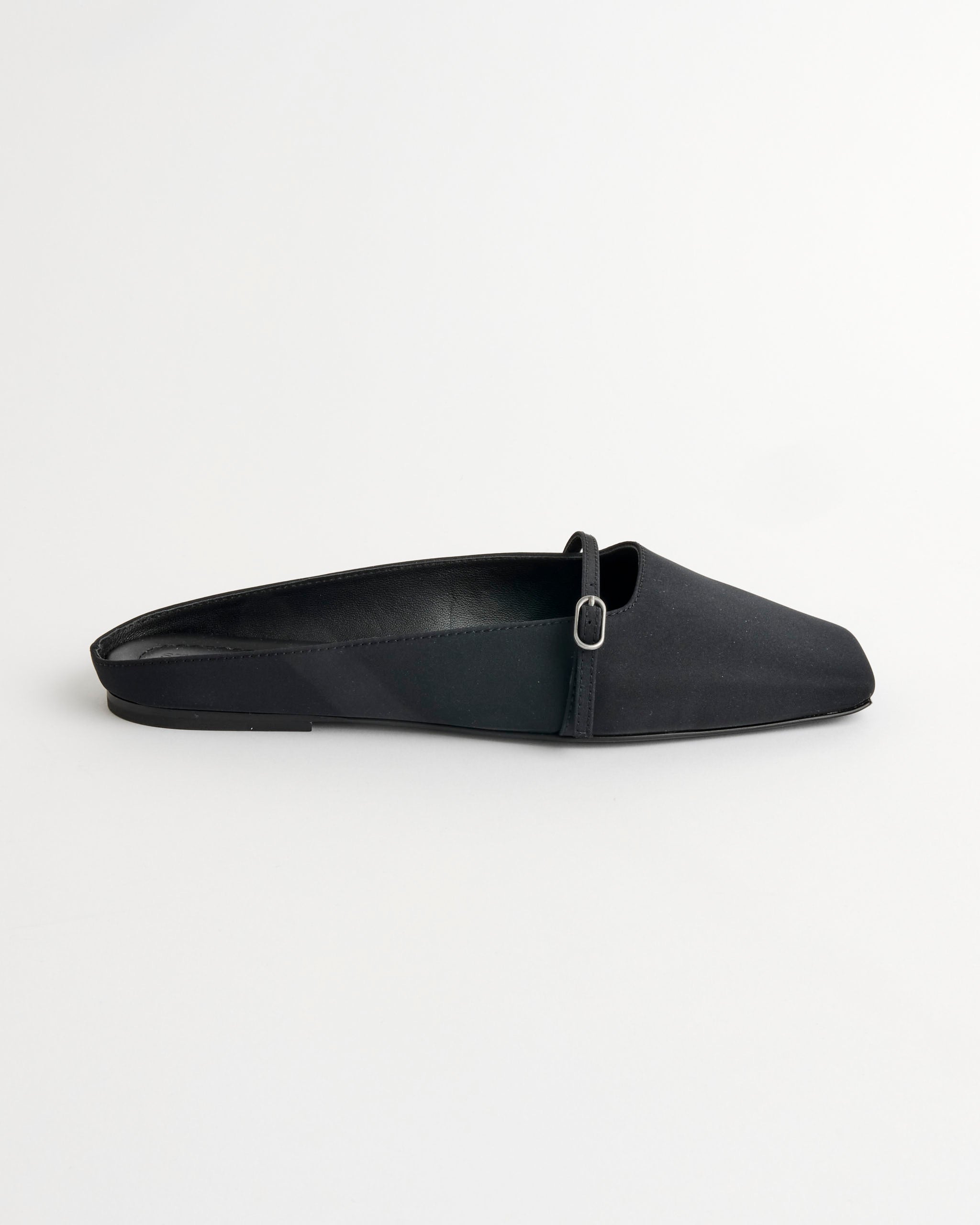 The ST. AGNI Plié Flat Shoes in Black feature a pointed toe, flat backless design, and a thin strap across the upper, shown against a plain white background.
