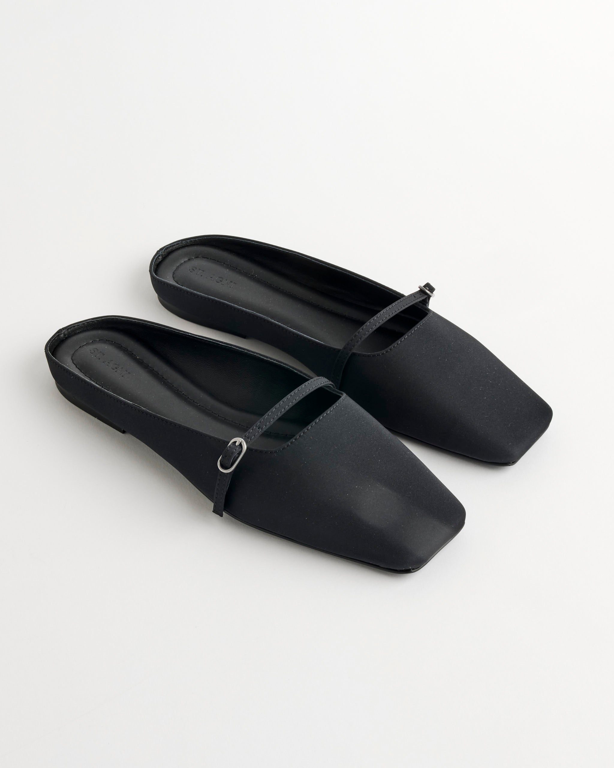 The ST. AGNI Plié Flat Shoes in Black feature a square toe, thin strap, and small buckle across the upper, shown on a white background.