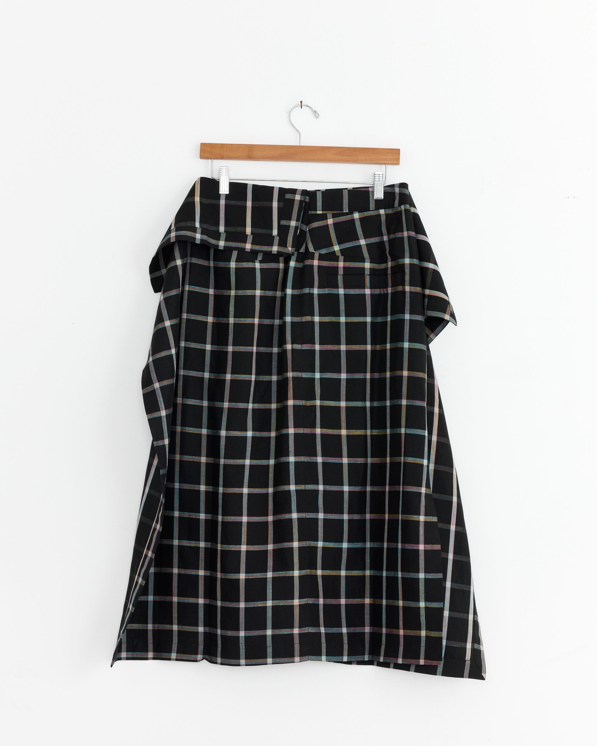 The Henrik Vibskov Ocu Skirt in Black Checks showcases a pastel plaid pattern on soft Tencel-linen blend, and is displayed on a wooden hanger against a white background.