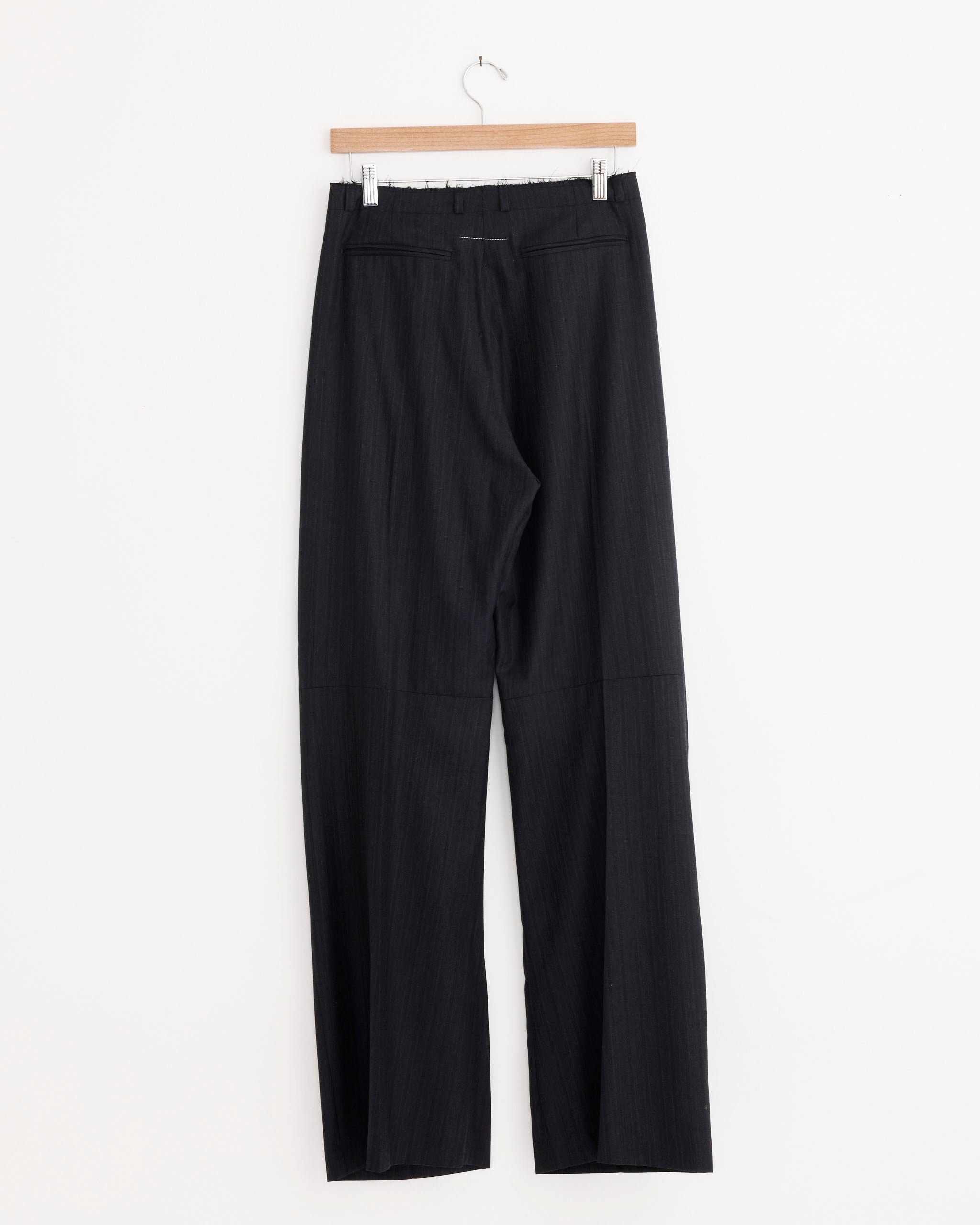 The MM6 Maison Margiela Pinstripe Wool Wide-Leg Trousers in Black hang on a wooden hanger against a plain white background.
