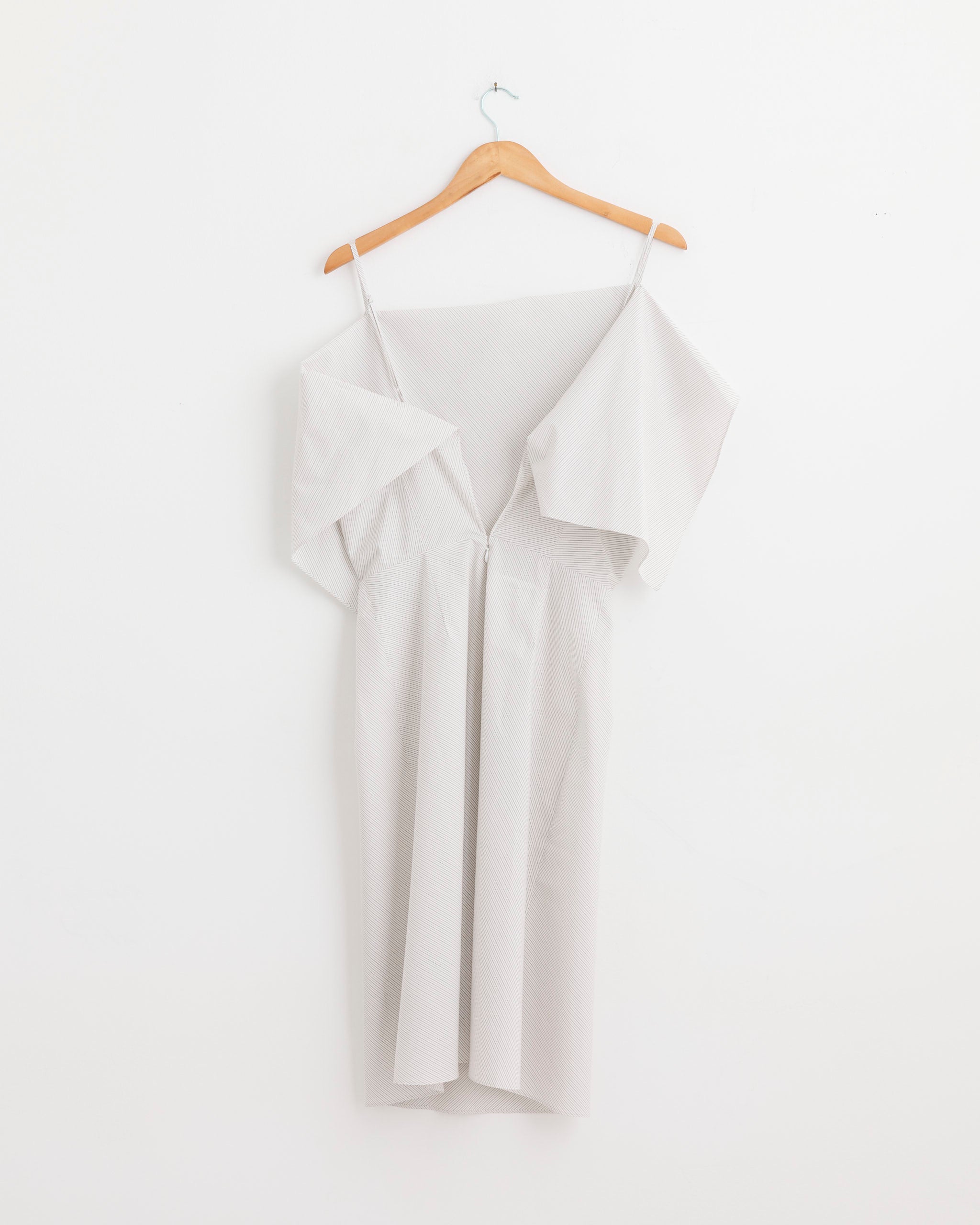 The MM6 Maison Margiela Midi Dress in White, featuring thin straps and a cotton off-the-shoulder design, hangs on a wooden hanger against a plain white wall.