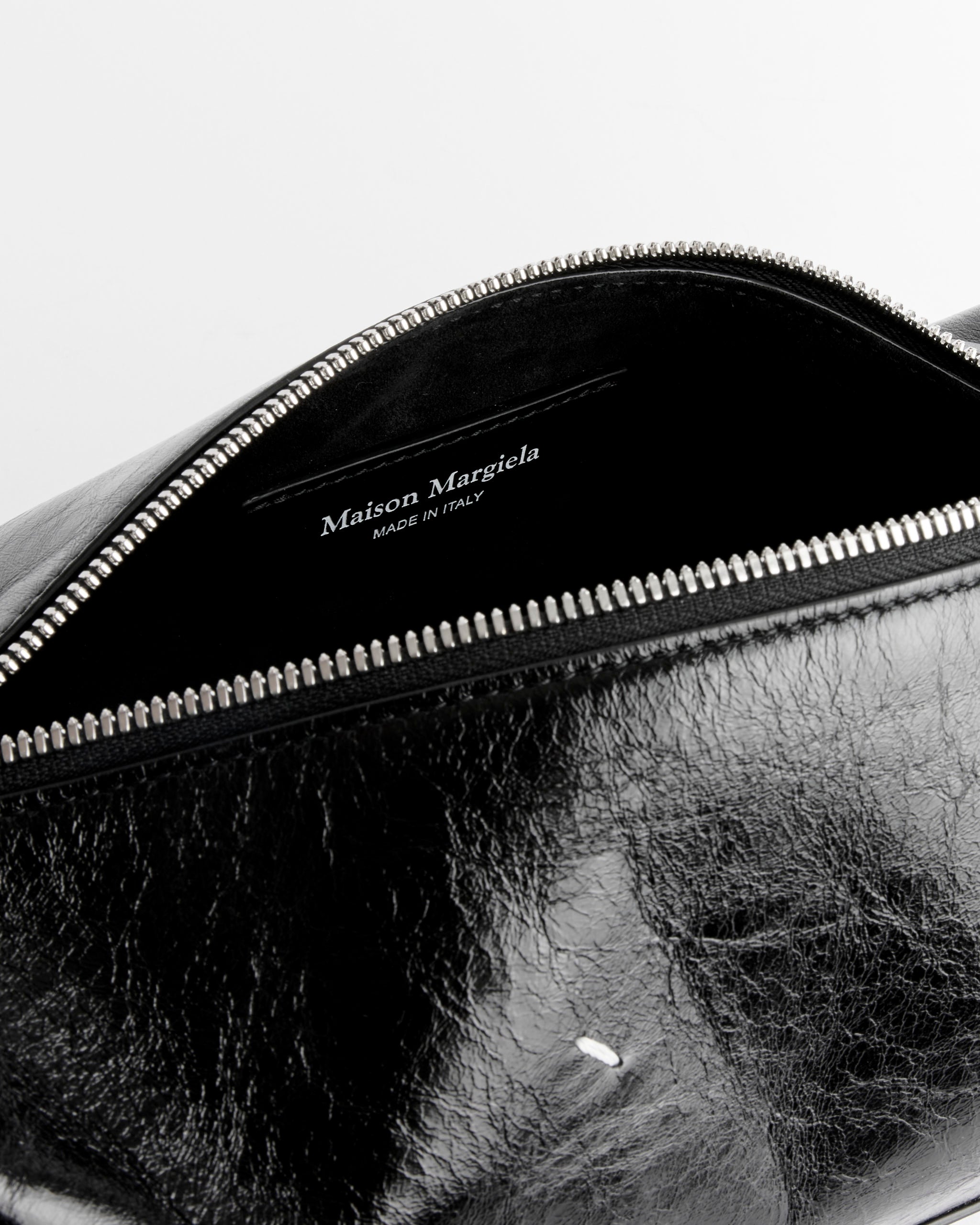 Close-up of the Maison Margiela Small Baguette Bag in black calf leather with a silver zipper partially open, showing an inner label reading "Maison Margiela MADE IN ITALY" in white on black lining.