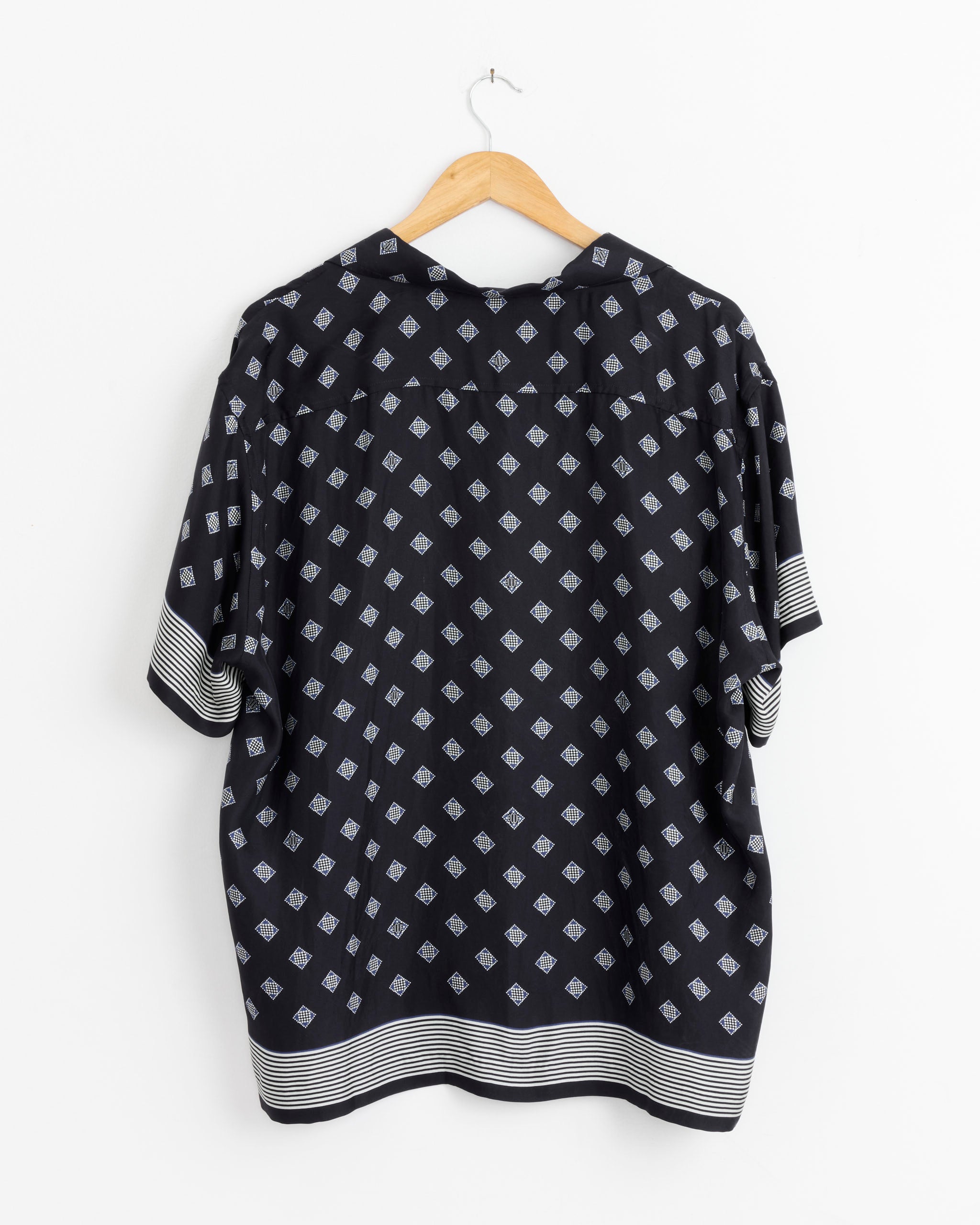The Bode Foyer Diamond Short Sleeve Shirt in Navy Blue features a stylish pattern of small white diamonds and horizontal white stripes on the cuffs and hem, elegantly displayed against a white background.