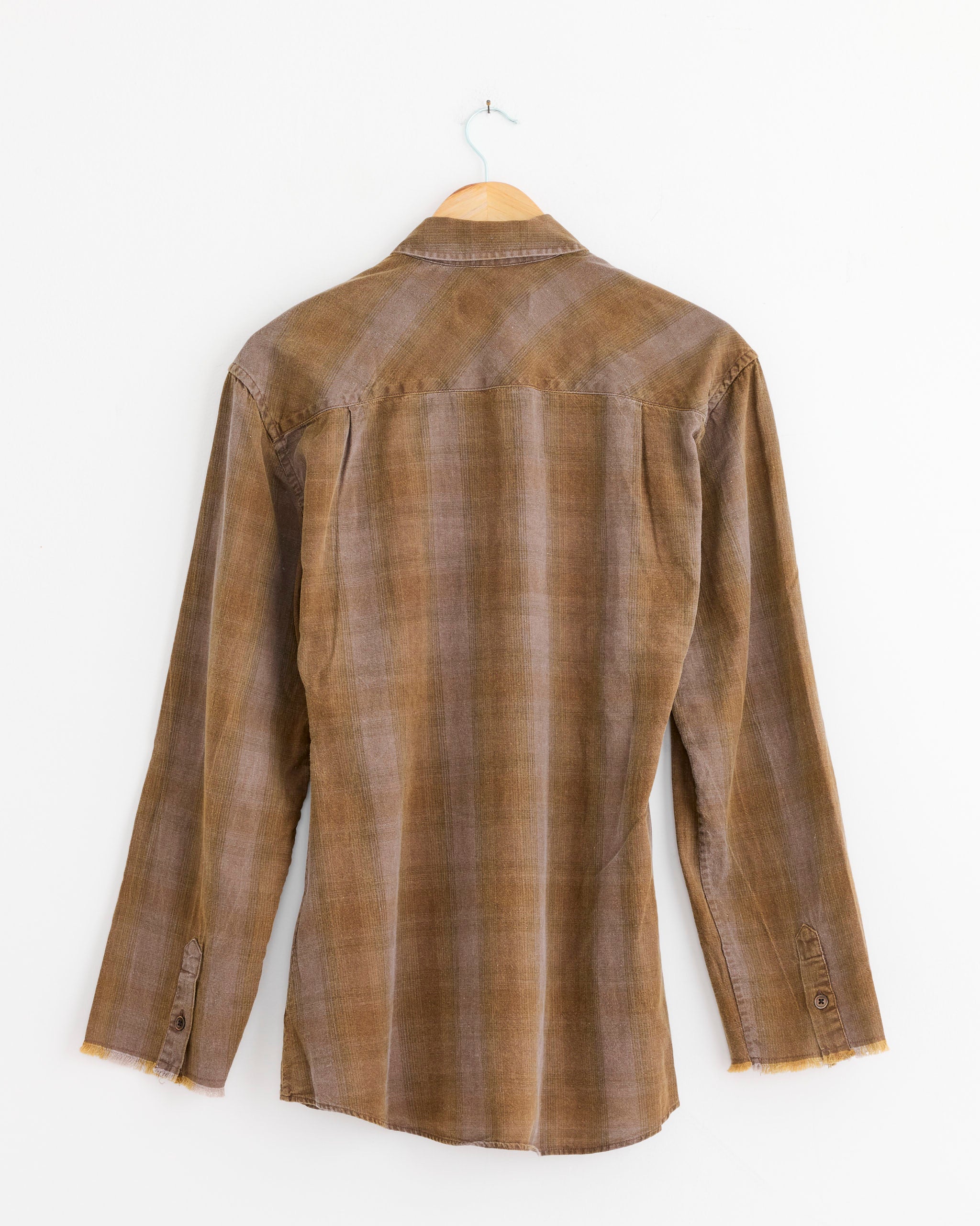 Back view of the Our Legacy Daisy Shirt in Dakota Flannel Check, featuring a collar, button cuffs, and raw hem in soft Portuguese cotton flannel, shown on a wooden hanger against a white background.