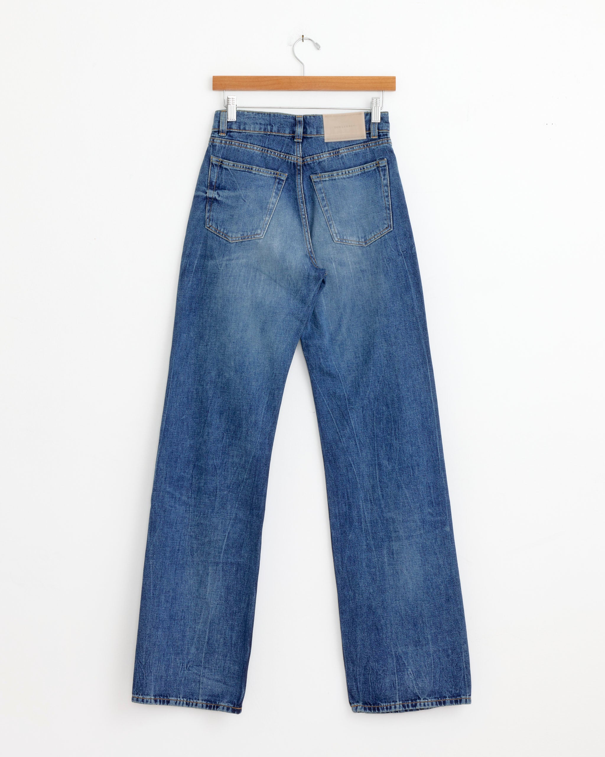 A pair of Our Legacy Wata Cut Jean in Vienna Blue Wash with straight legs, displayed from the back on a wooden hanger against a white background.