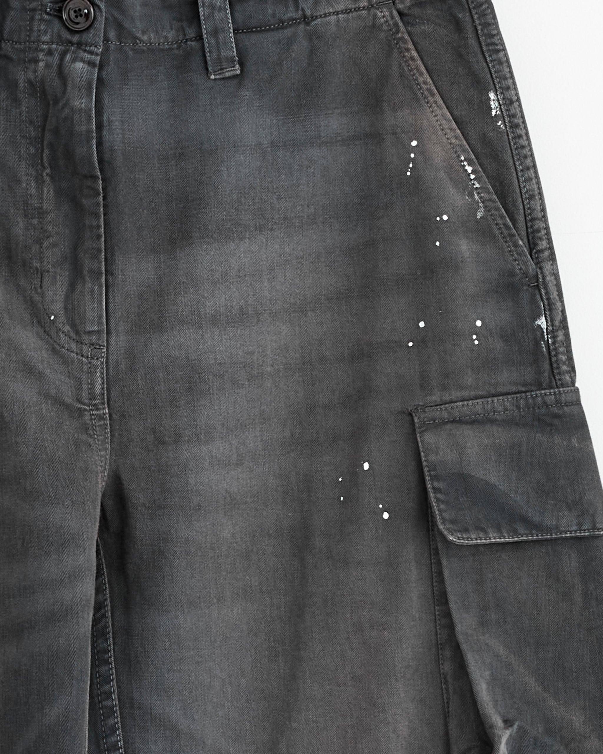 Close-up of Our Legacy’s Peak Cargo Pant in Nebula Wash, crafted from Italian cotton herringbone with a buttoned waistband, cargo side pockets, and subtle white paint splatter details.