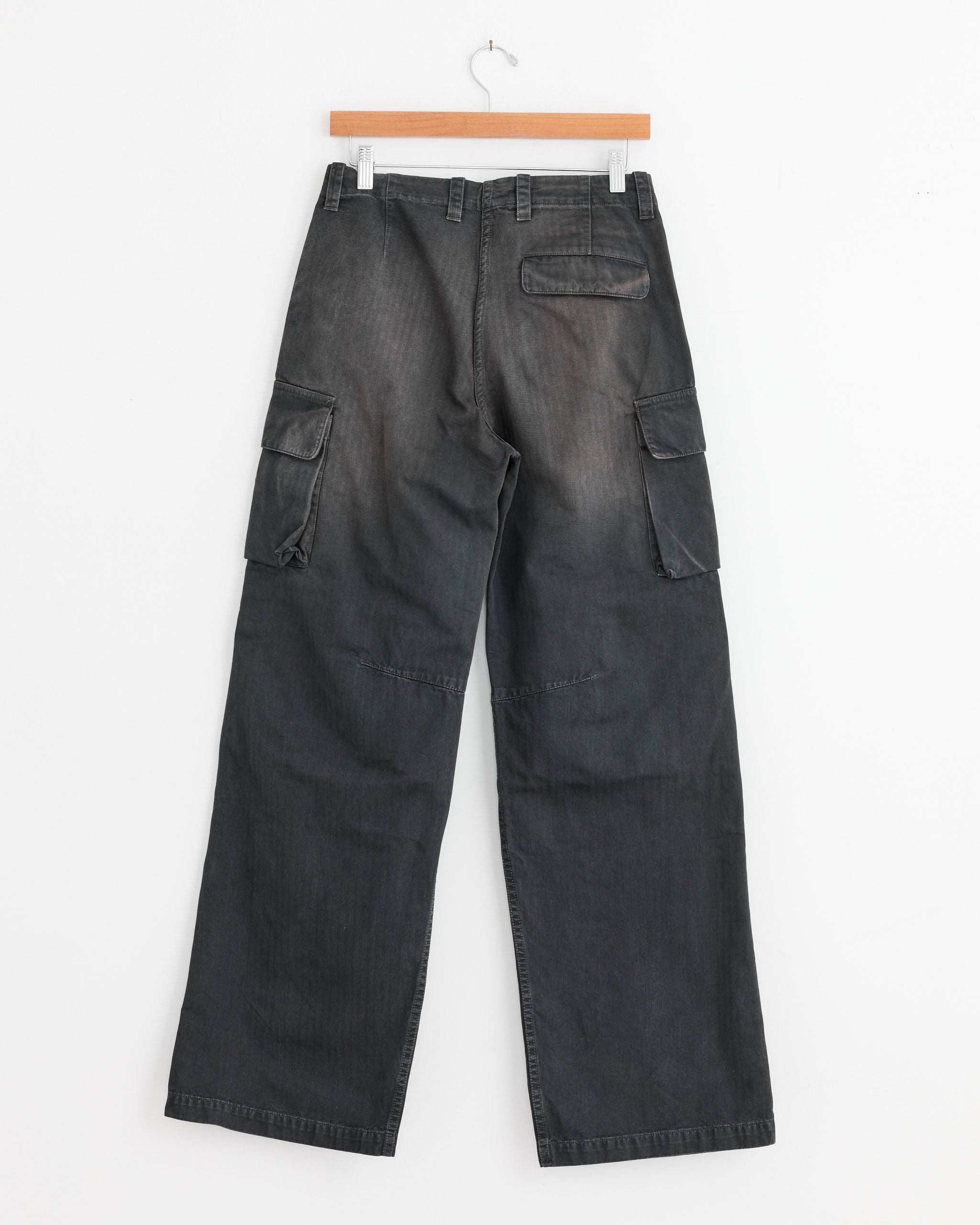 The Our Legacy Peak Cargo Pant in Nebula Wash, made from Italian cotton herringbone with cargo side pockets and a single back pocket, hangs on a wooden hanger against a white background.
