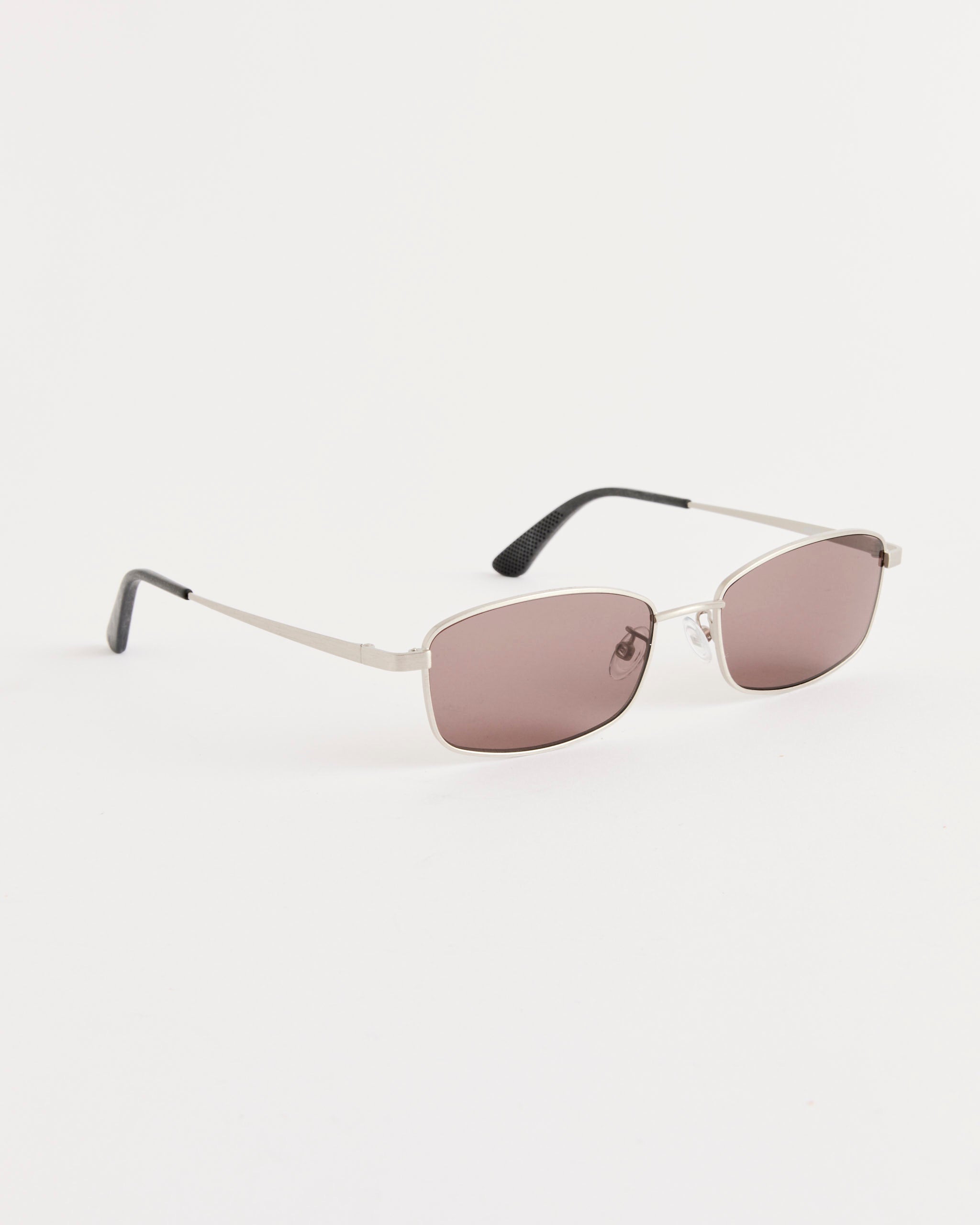 Our Legacy’s Librarian Sunglasses in Silver Hawk feature a sleek German silver rectangular frame, light brown tinted lenses, and black ear tips, displayed on a plain white background.