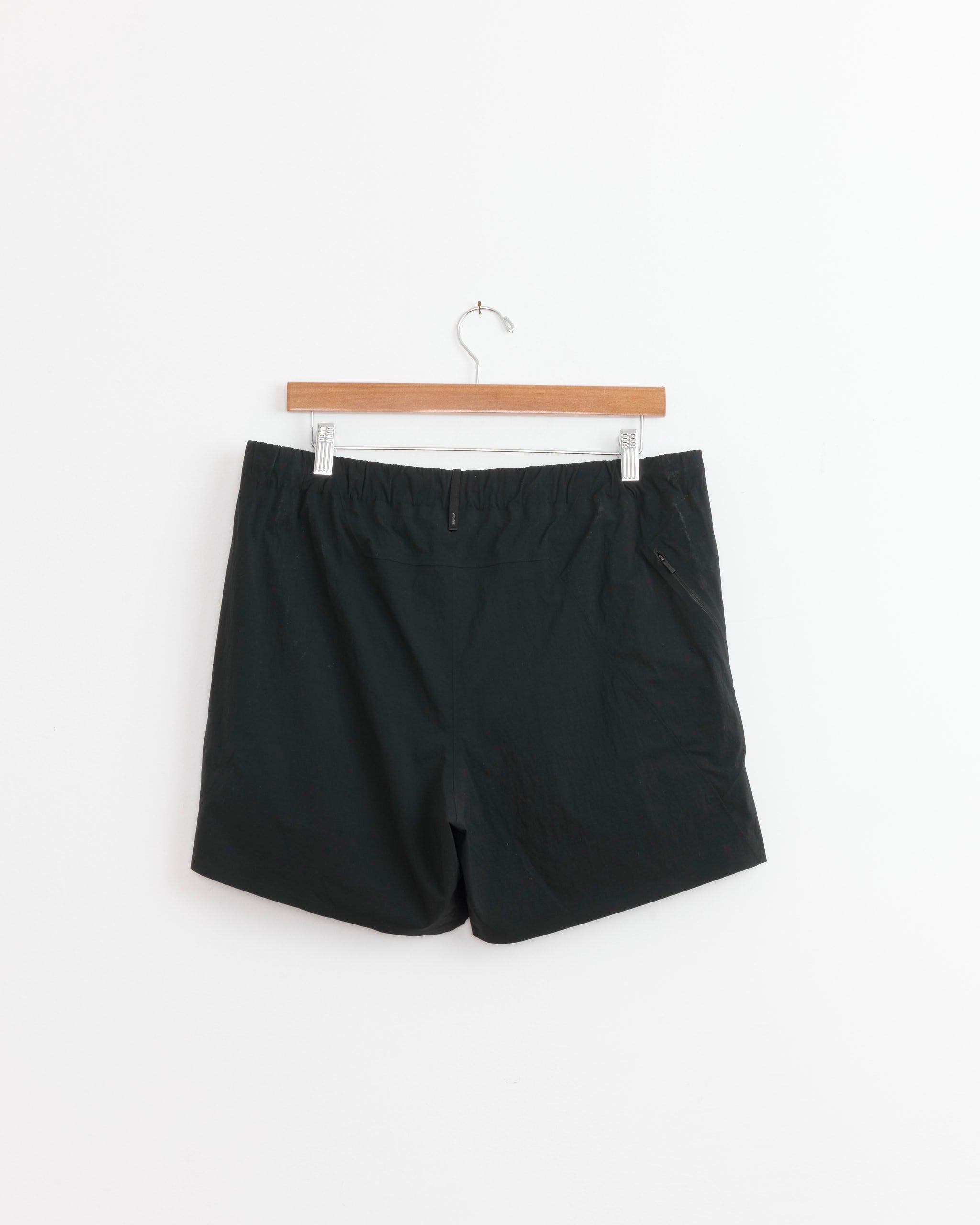 The Veilance Argand Short in Black, a lightweight performance short, is displayed hanging on a wooden hanger against a plain white background.