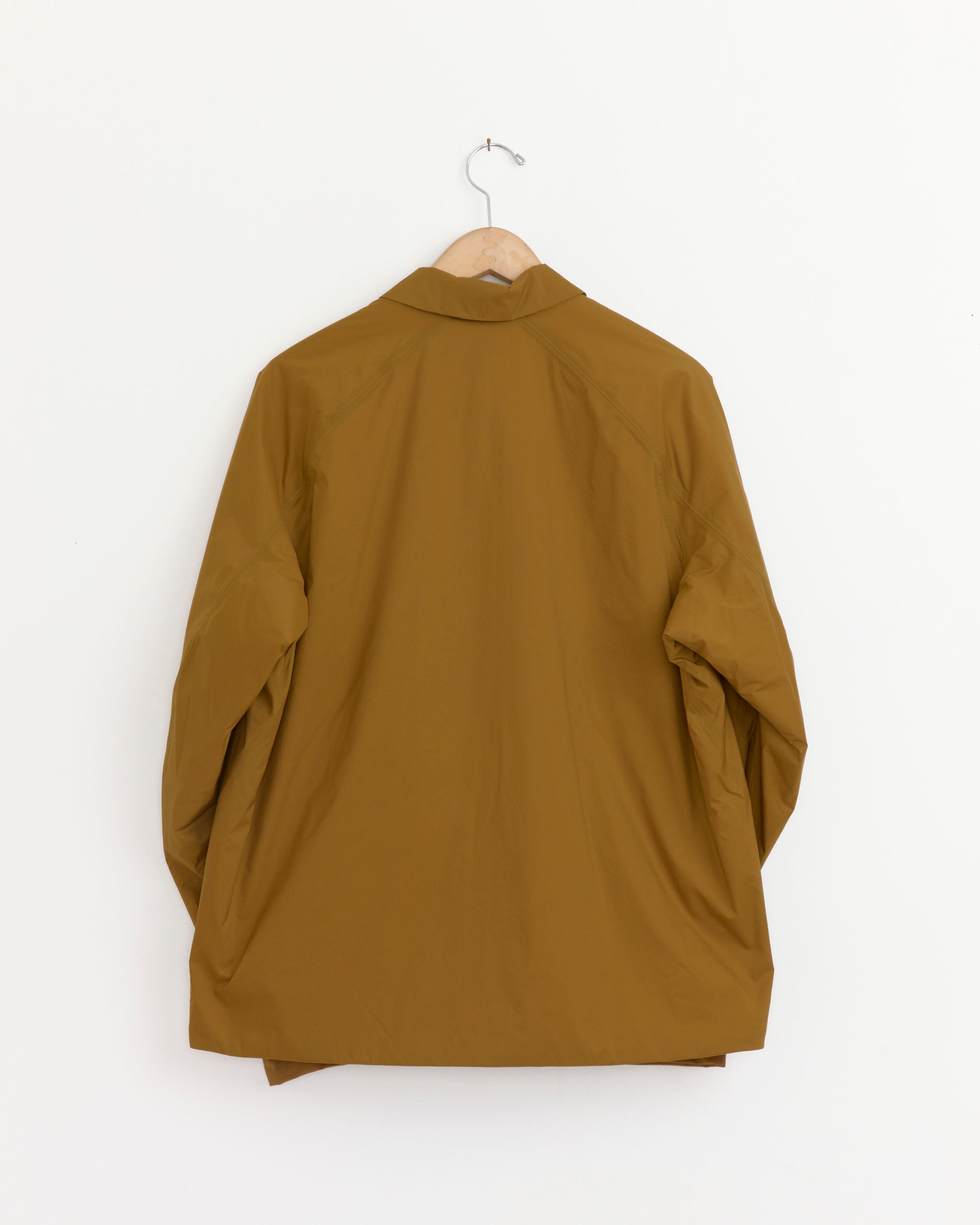 The Veilance Demlo Insulated Jacket in Relic, shown from the back on a simple metal hook against a white wall—ideal for those wanting detailed fit or sizing info via online chat.