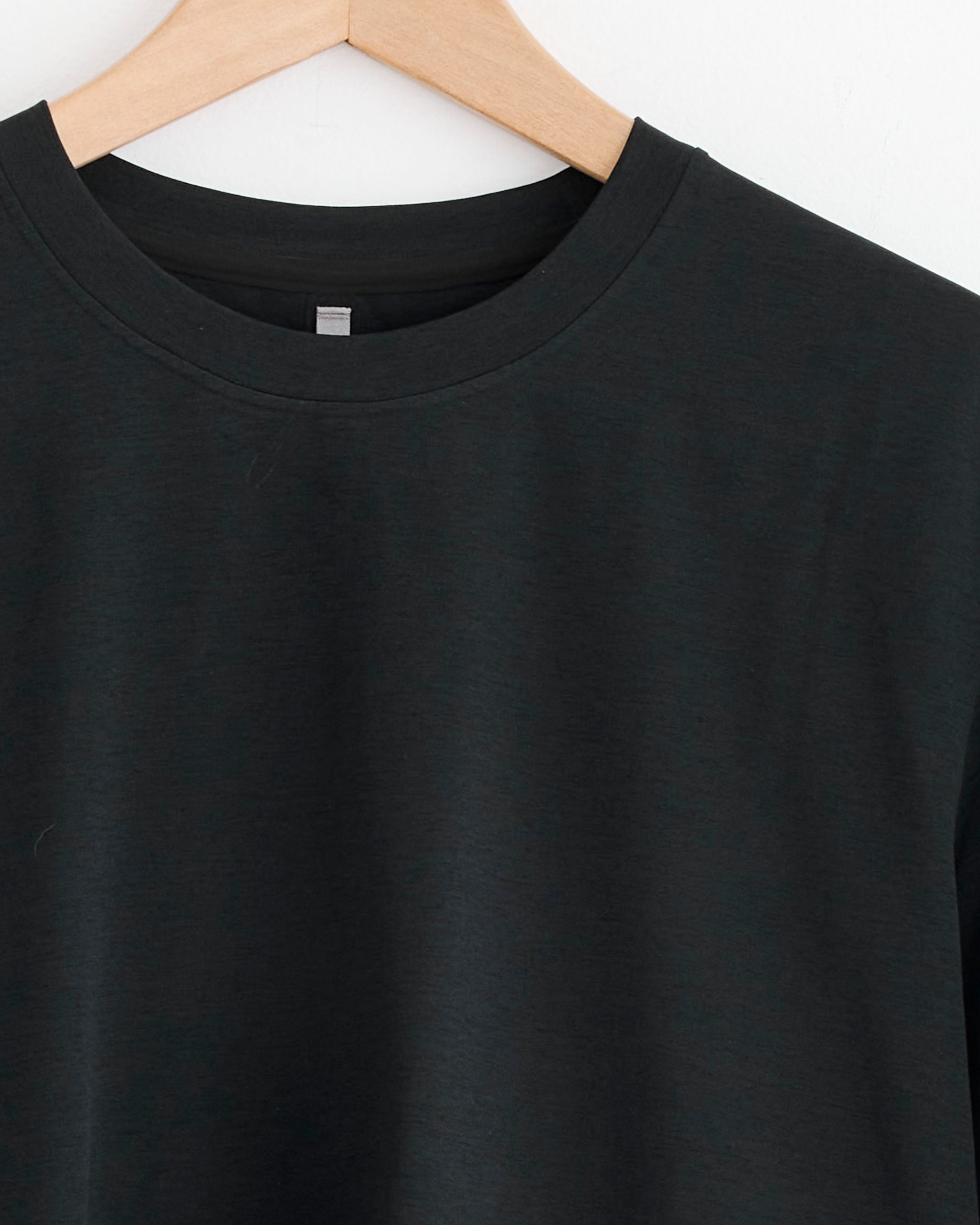 The Veilance Metron Tee in Black, a classic crew-neck t-shirt, hangs on a wooden hanger against a white background—ideal for easy sizing and a comfortable fit.