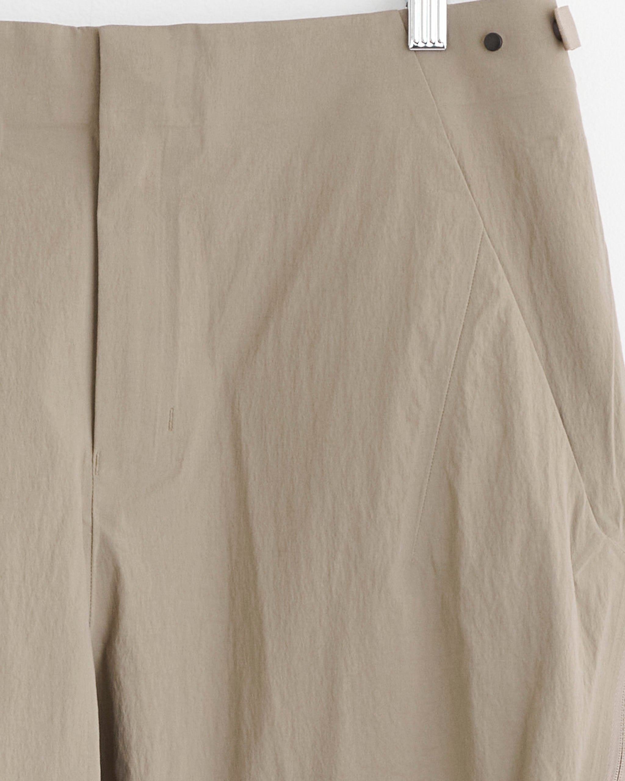 The Veilance Spere Cargo Pant in Lt Gnosis features a high waist, relaxed fit, hidden zipper, slanted side pocket, and lightly crinkled beige fabric. Shown hanging on a white hanger. For sizing help, use our online chat.