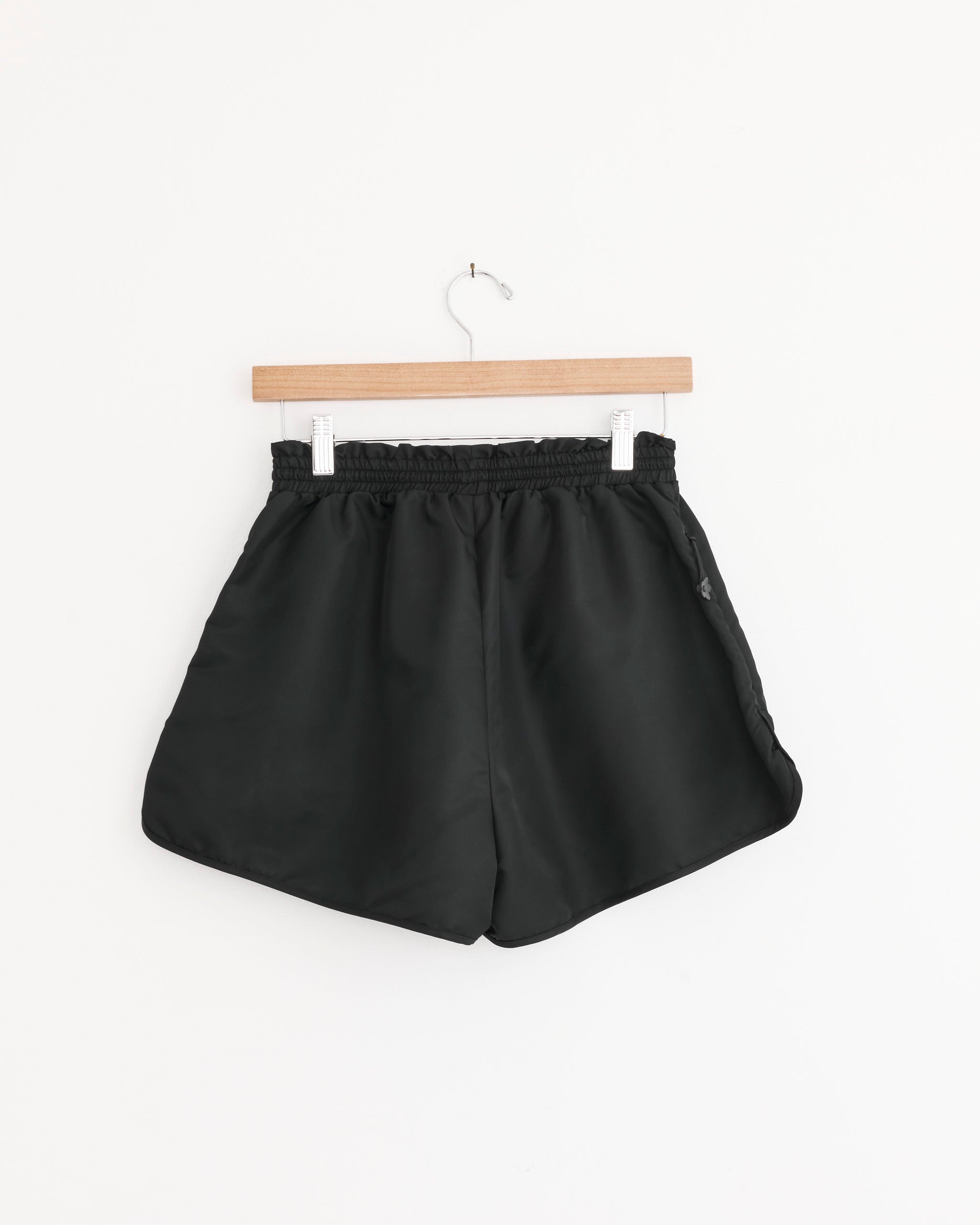 The Cecilie Bahnsen Colette Short in Black, featuring an elastic waistband, hangs on a wooden hanger against a plain white background.