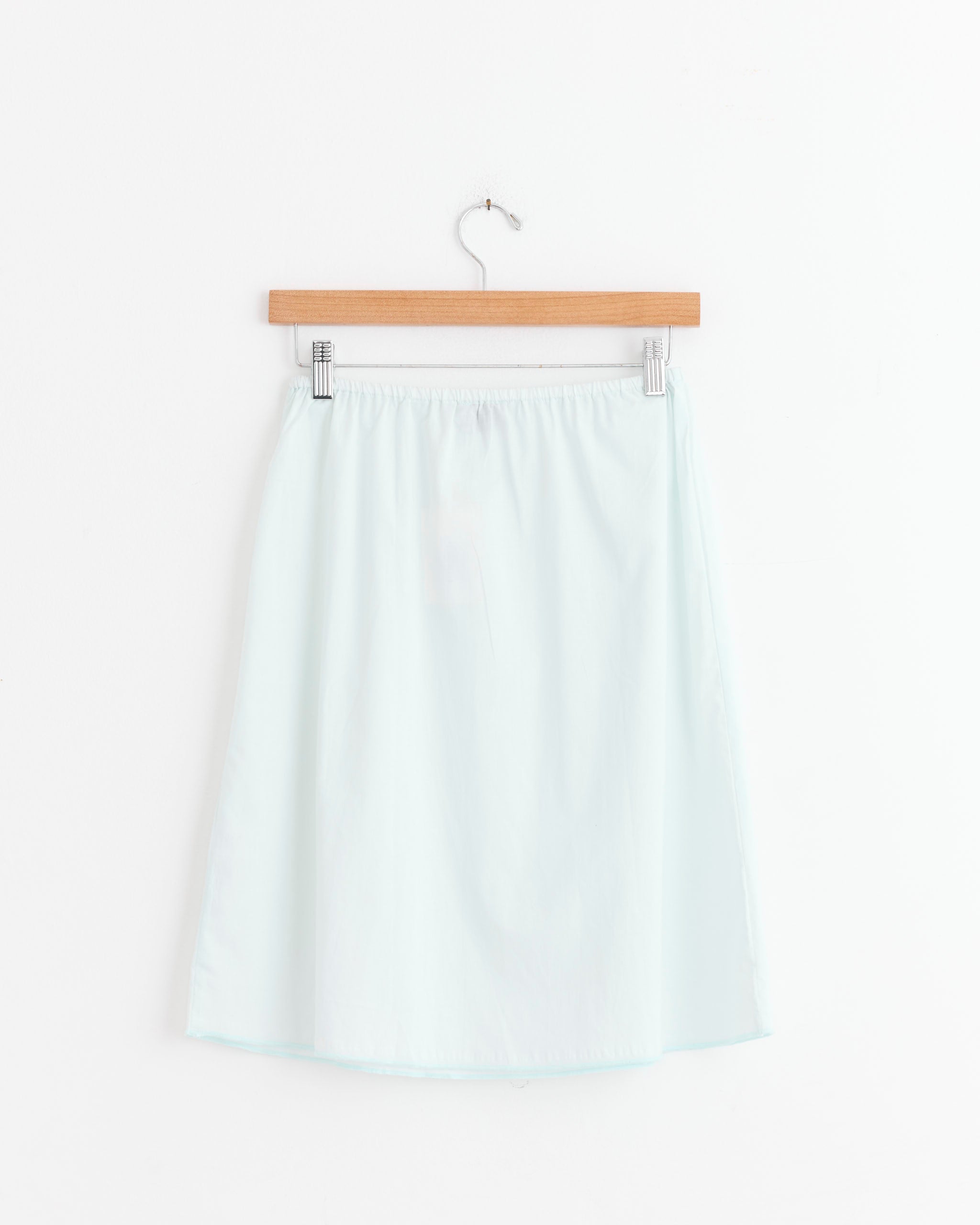 The Simple Skirt in Mint by Deiji Studios, featuring a flattering A-line silhouette in light blue, is displayed on a wooden hanger against a plain white background.