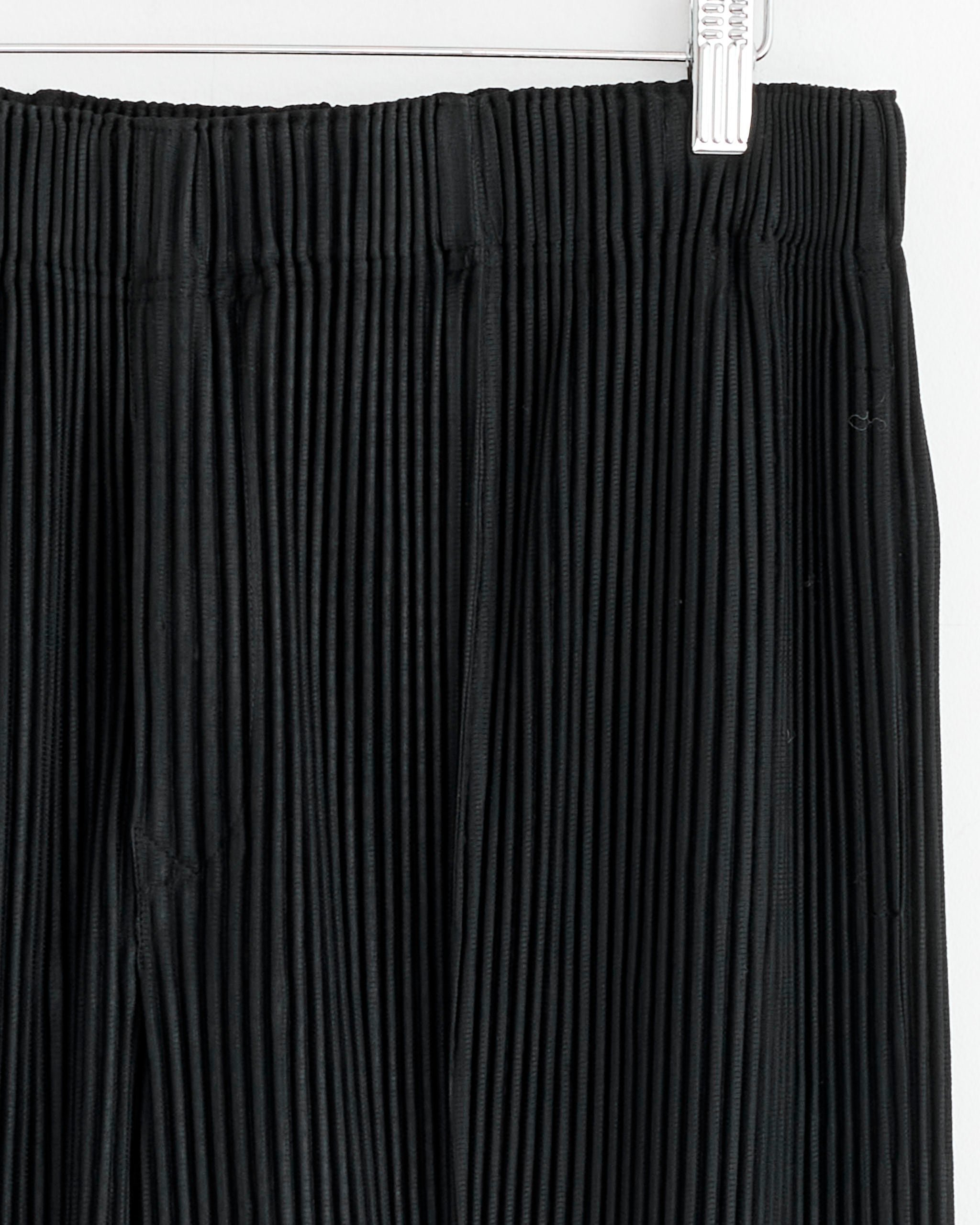 Close-up of the waistband and upper section of the Homme Plissé Issey Miyake MC January Pant in Black, hanging on a white hanger against a white background.