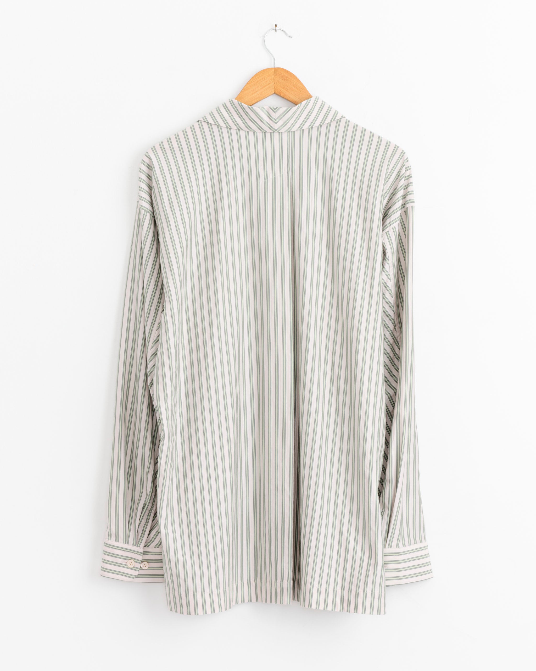 A Homme Plissé Issey Miyake Stripe Jersey Shirt in Green with an Italian collar is shown from the back, hanging on a wooden hanger against a white wall.