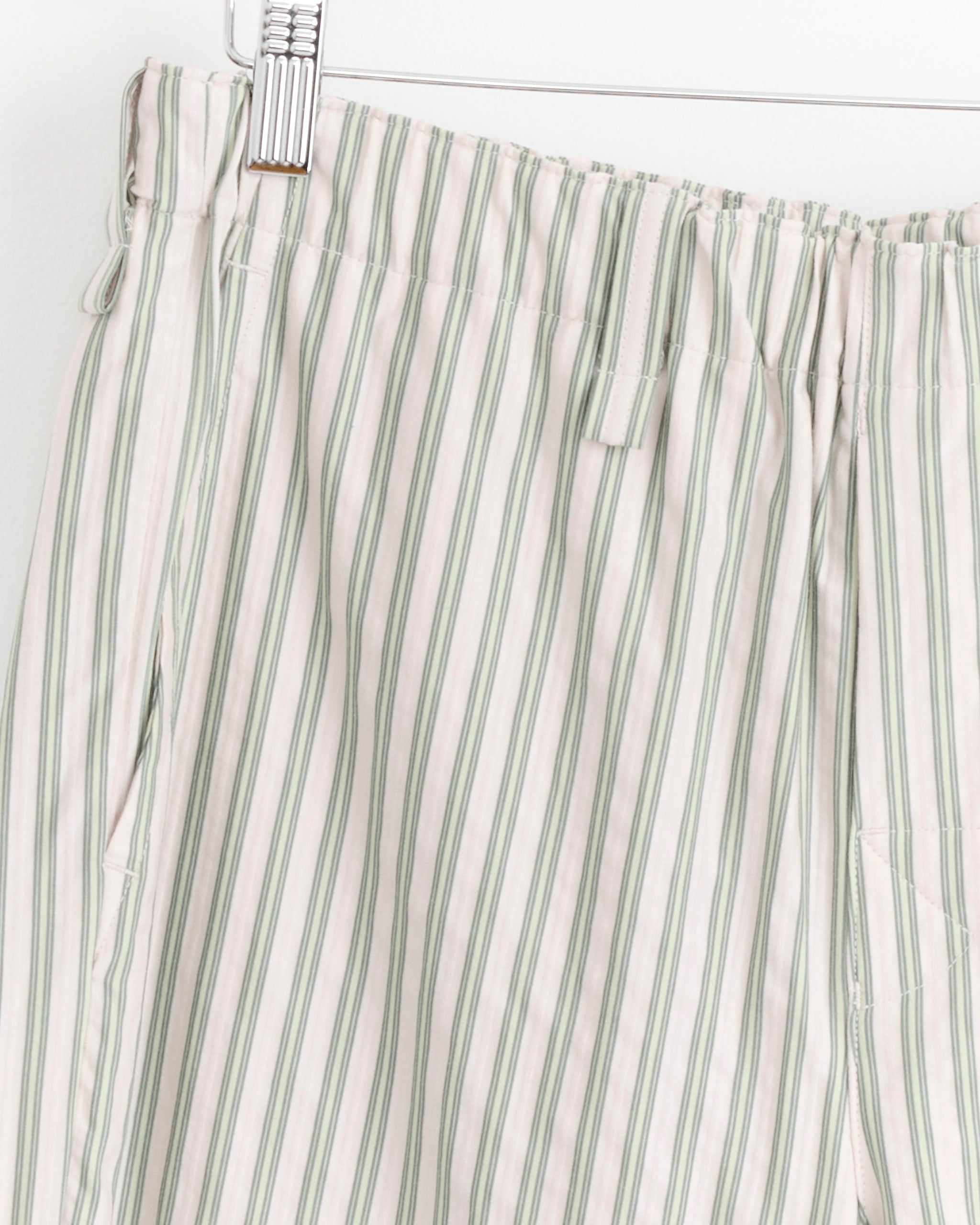 Close-up of the Stripe Jersey Short in Green by Homme Plissé Issey Miyake, showcasing vertical green and white stripes, elastic waistband with drawstring, and side pocket, displayed on a hanger against a white background.