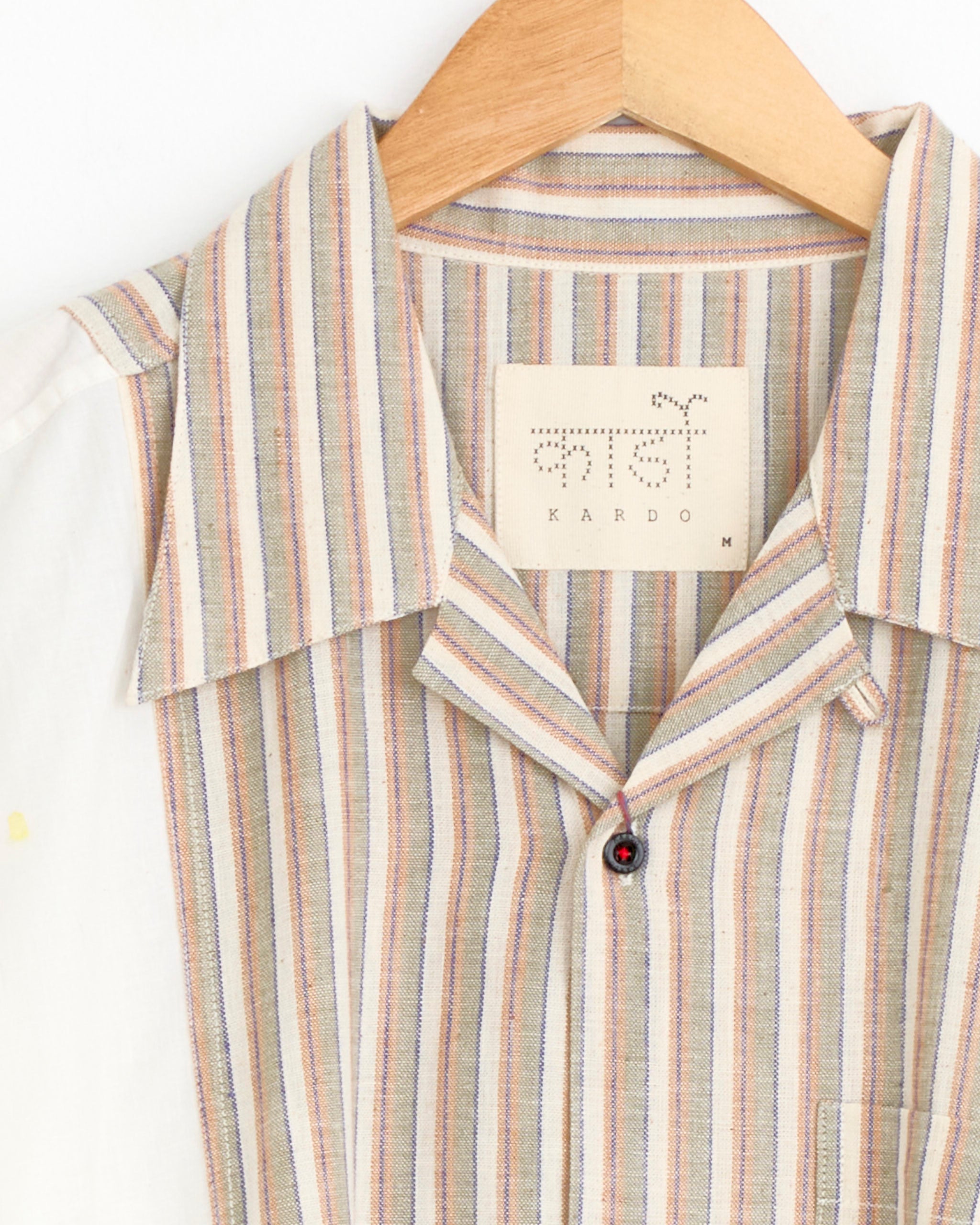 A close-up of the Kardo Kunal Shirt in Multi, a handwoven collared shirt with vertical beige, blue, red, and yellow stripes, hanging on a wooden hanger with the Kardo label visible inside the collar.