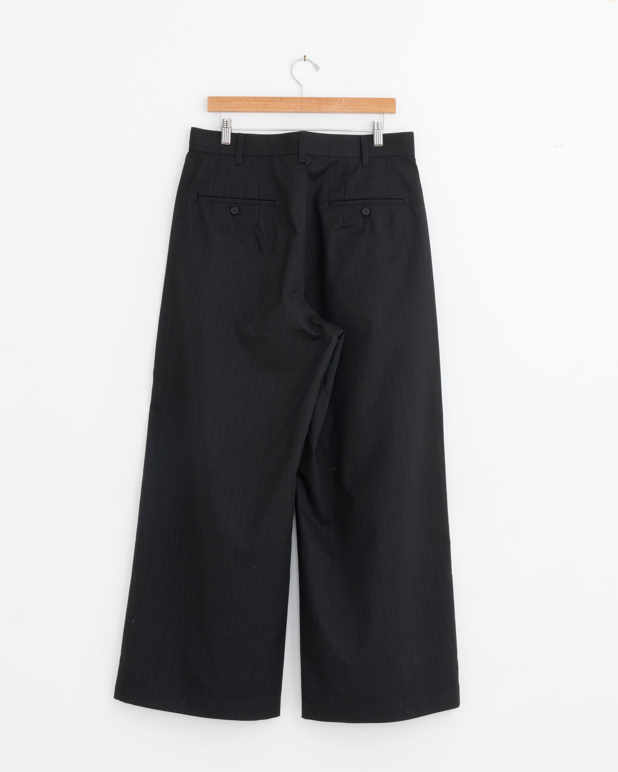 The Comme Des Garçons Homme 005 Pant in Navy, made from a Japanese polyester wool blend, features a wide-leg cut and two buttoned rear pockets, displayed on a wooden hanger against a white background from the back.