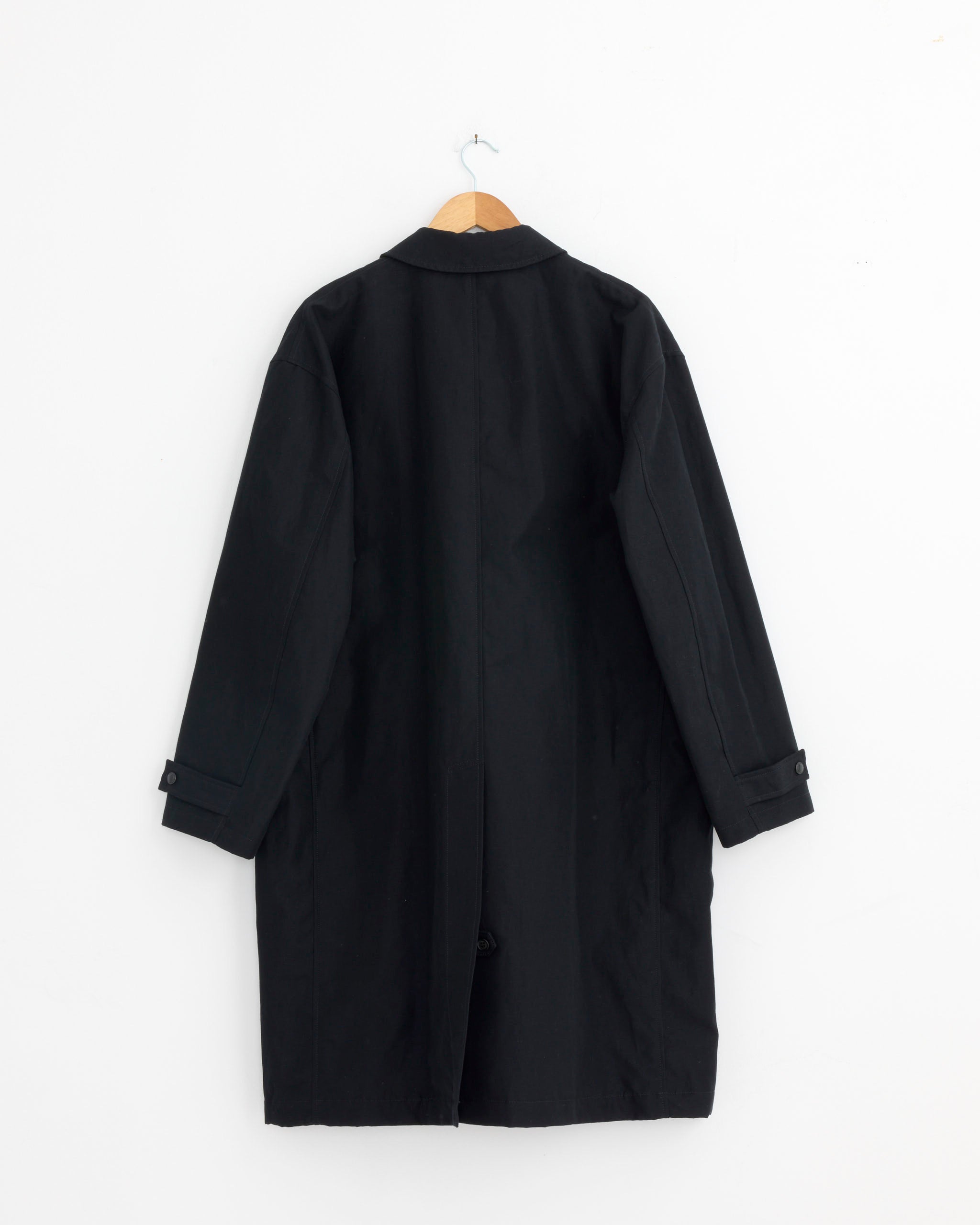 The Comme Des Garçons Homme 001 Coat in Navy, made in Japan, hangs on a wooden hanger against a plain white wall, displayed from the back.