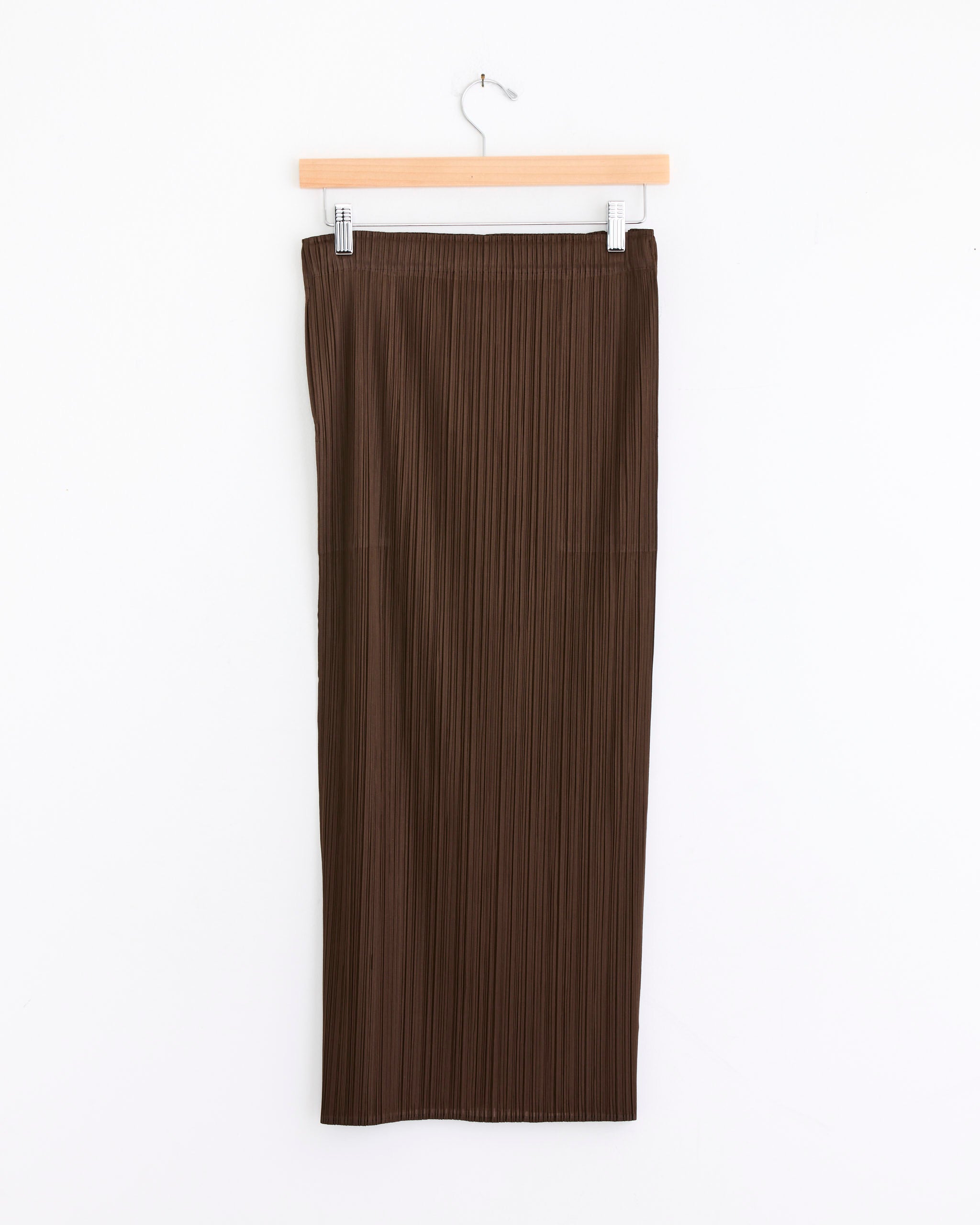 The NC Basics 4 Skirt in Brown by Pleats Please Issey Miyake hangs elegantly on a wooden hanger against a plain white background.