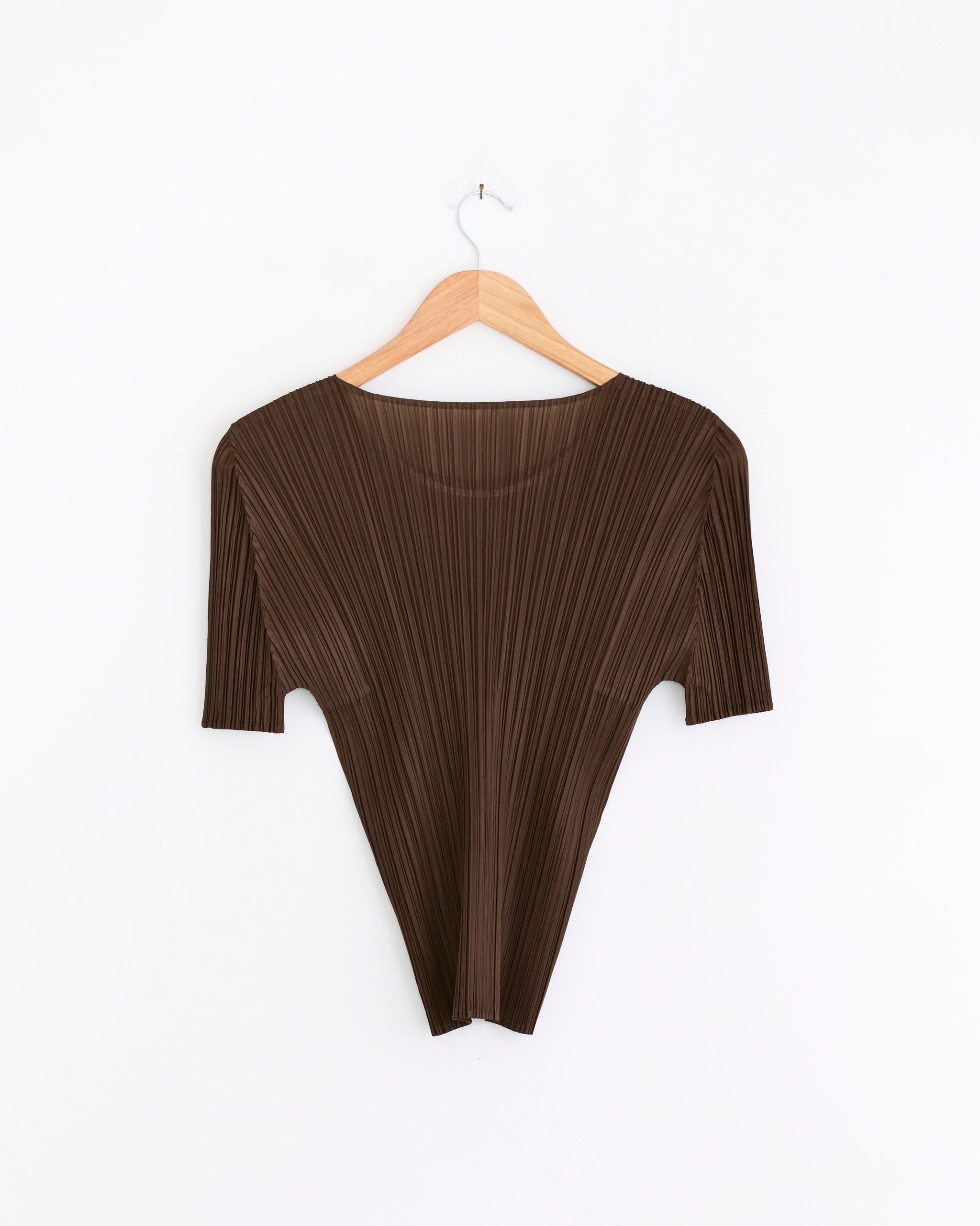 The NC Basics 4 Top in Brown by Pleats Please Issey Miyake, made from lightweight polyester, has a pleated finish and features an angular silhouette with wide shoulders and a narrow bottom. It is displayed on a wooden hanger against a white background.