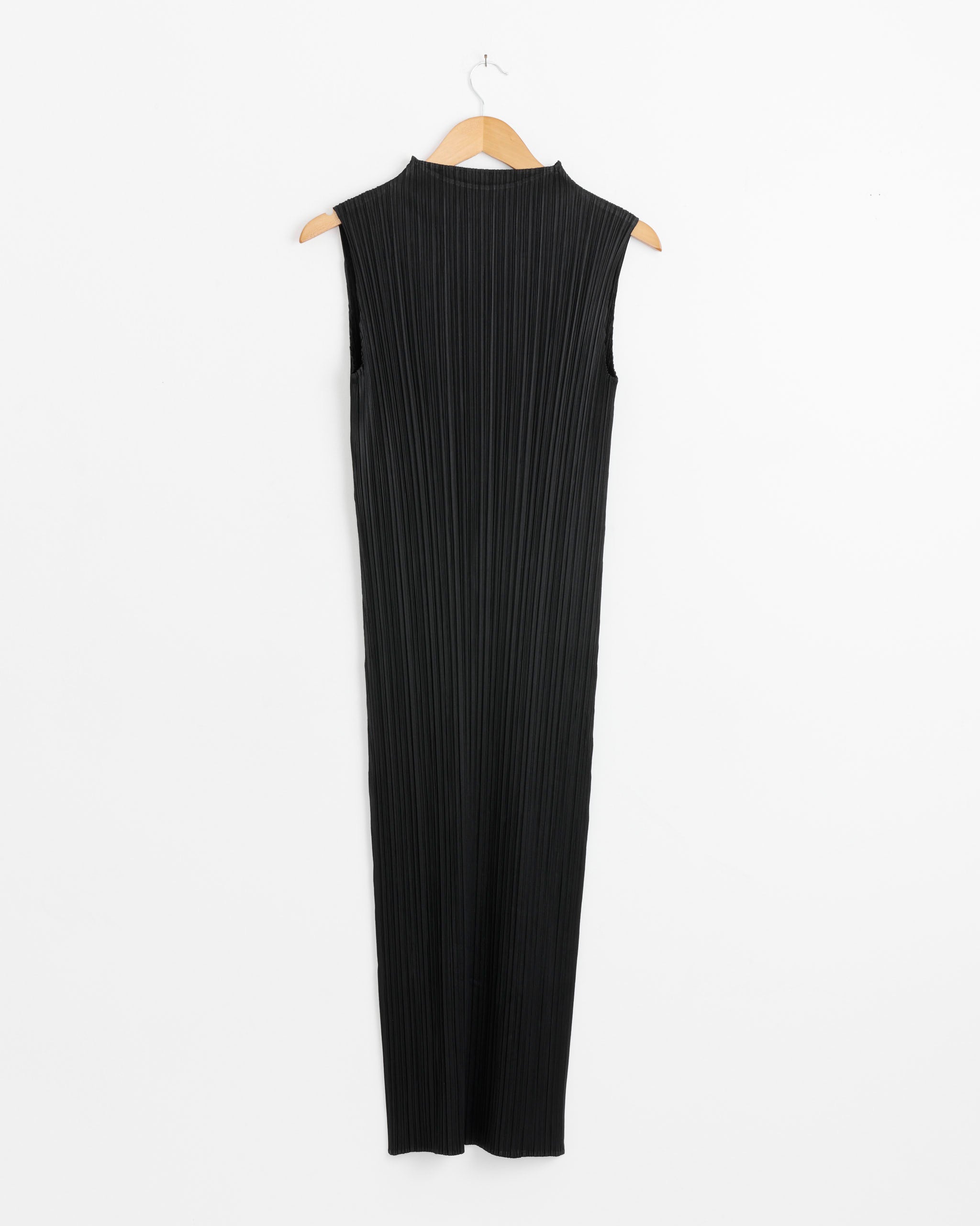 The MC April Dress in Black by Pleats Please Issey Miyake is a sleeveless, high-collared dress with vertical pleats and no visible fastenings, displayed on a wooden hanger against a plain white background.