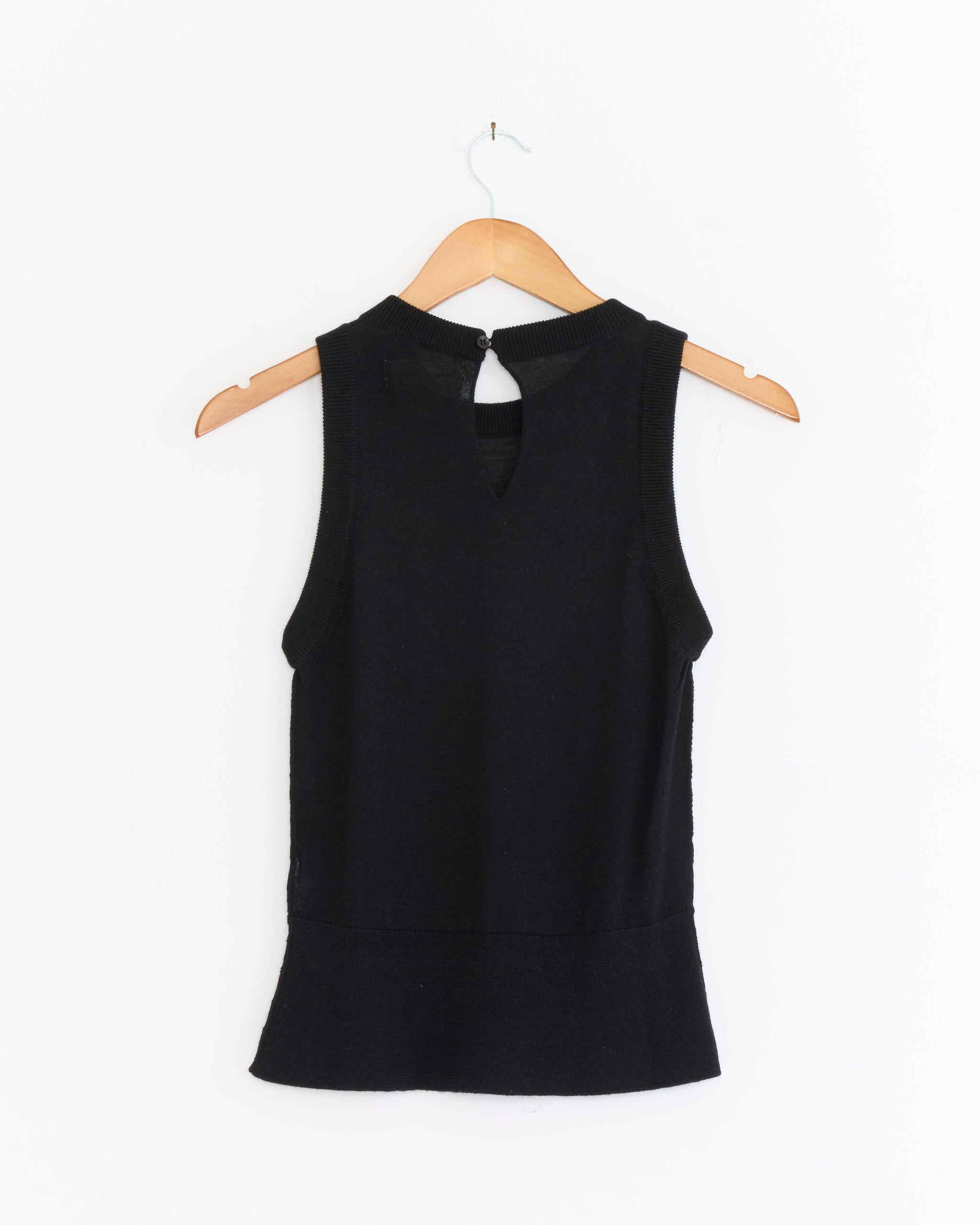 The mfpen Appointment Top in Black—a sleeveless wool-silk blend with a back keyhole—hangs on a wooden hanger against a plain white background.