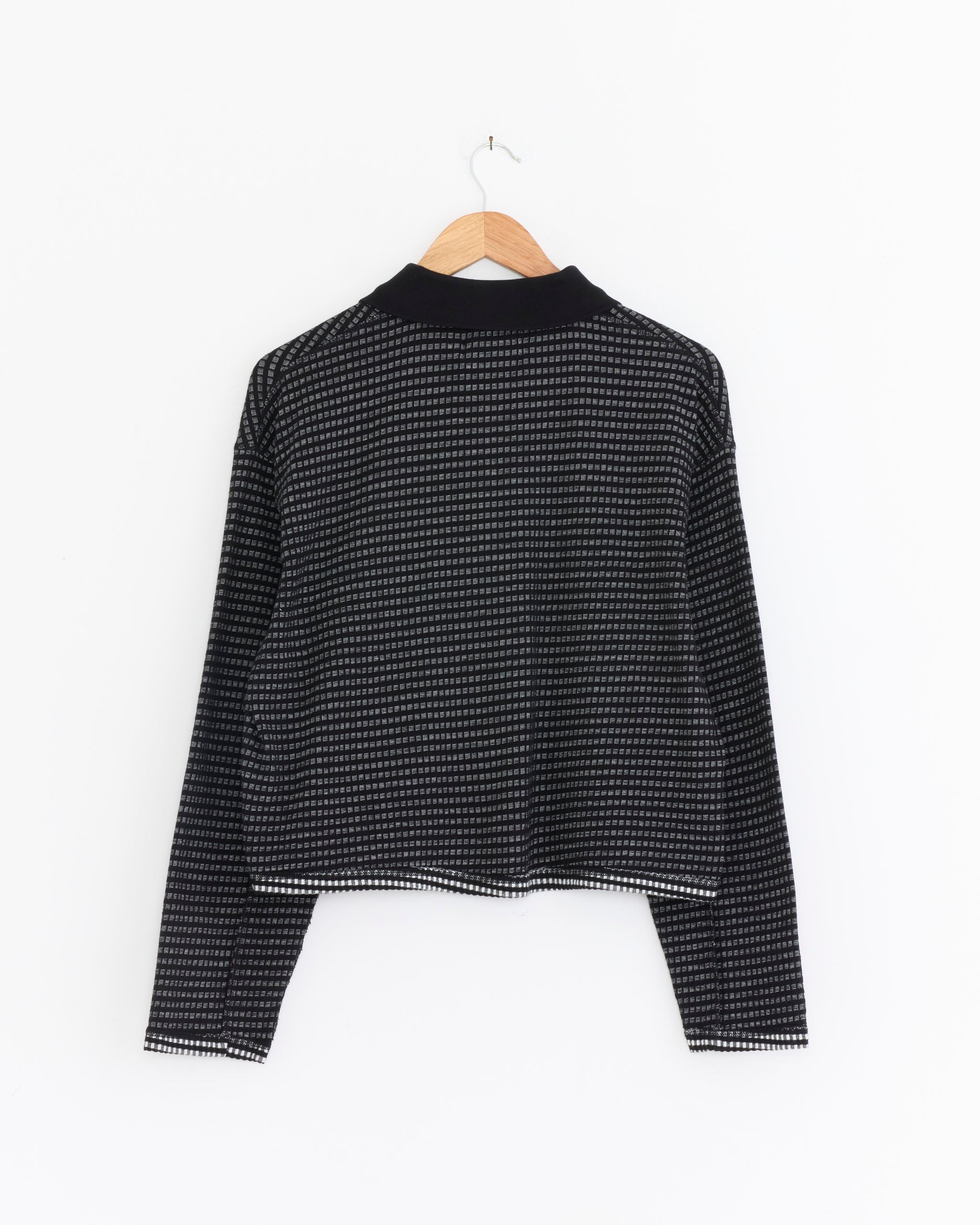 The mfpen Cropped Polo Top in Black is displayed from the back, featuring a jacquard check pattern in black and white. It hangs on a wooden hanger against a plain white background.