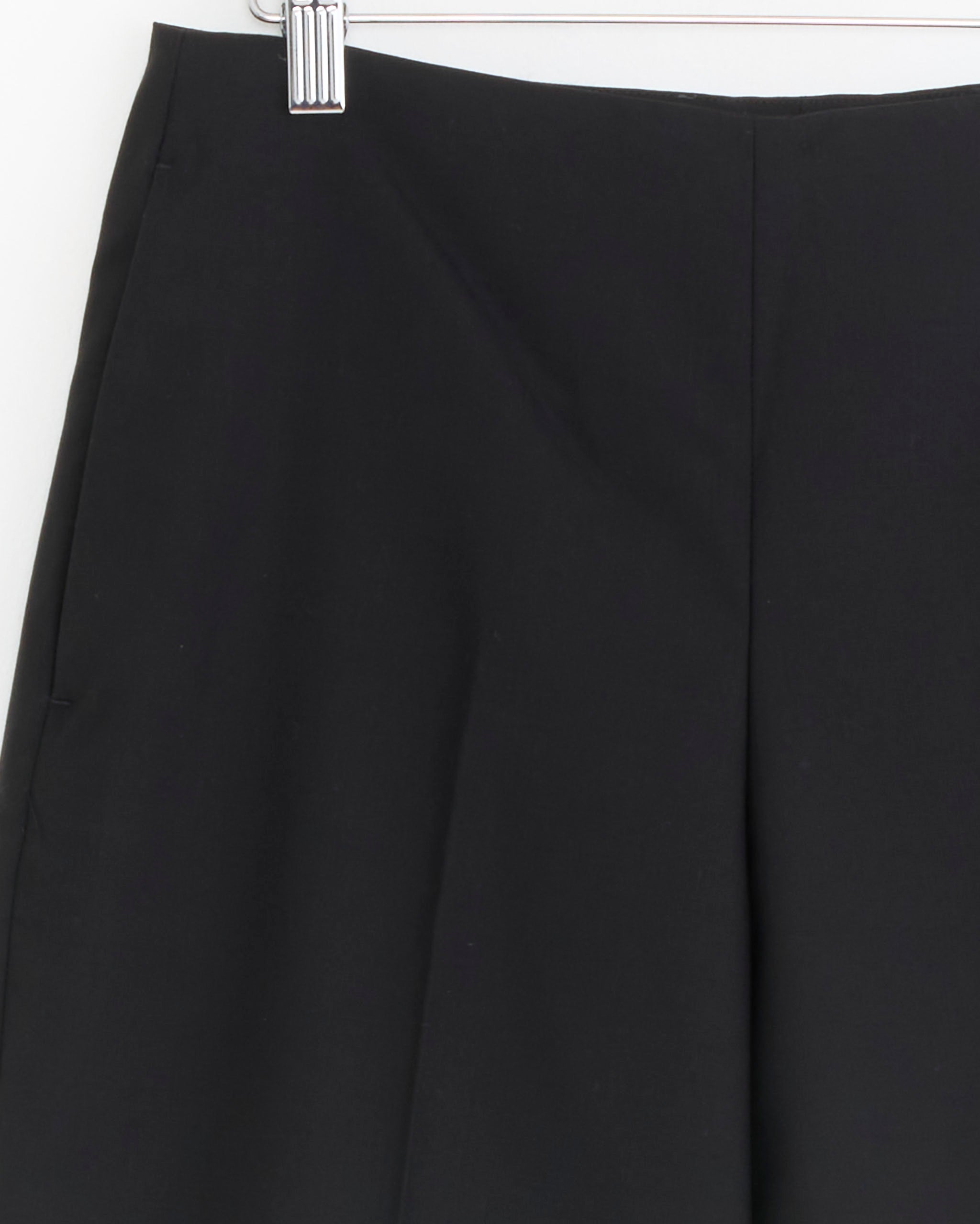 Close-up of the mfpen Taper Trouser in Black, crafted from tropical wool. The photo shows the upper section and waistband hanging on a hanger against a white background.