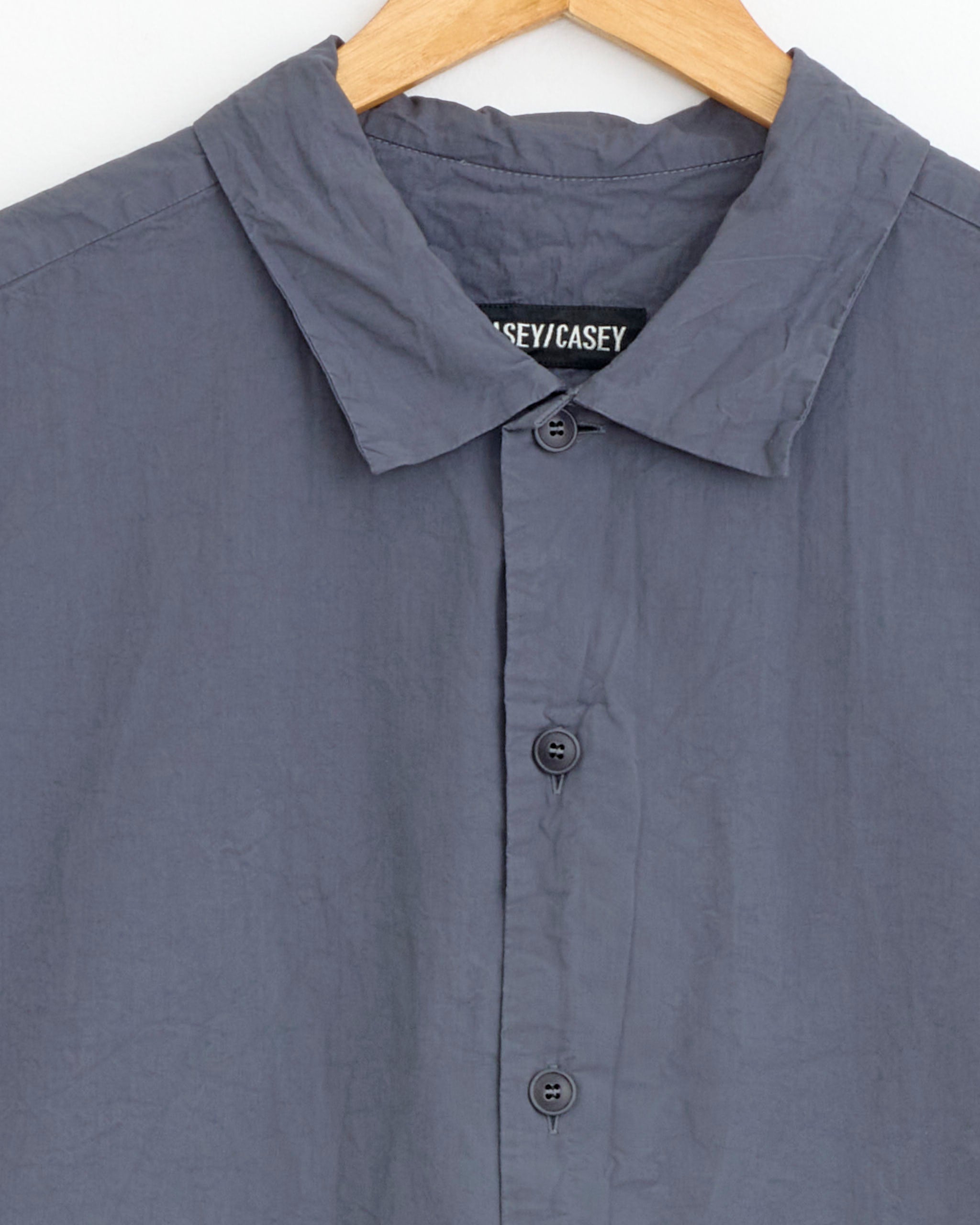 A close-up of the Mili Volume Shirt in Grey by Casey Casey, shown on a wooden hanger with four visible buttons and a CASEY/CASEY label inside the collar.