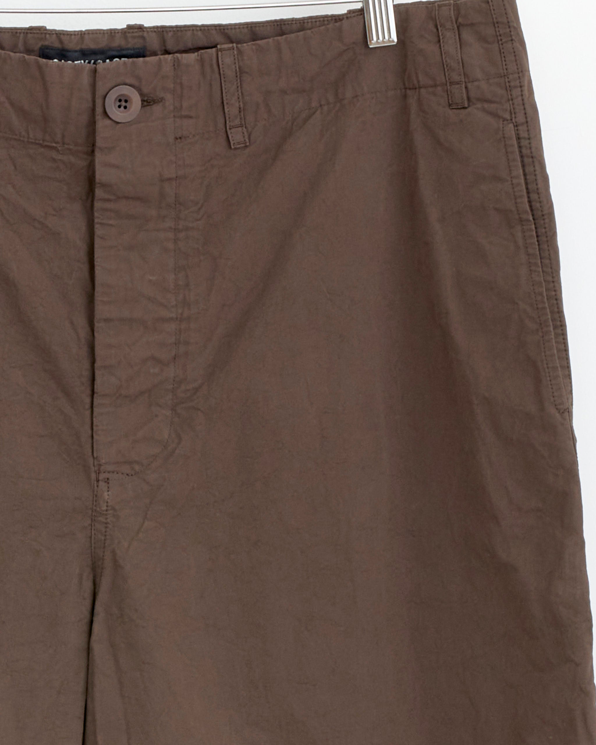 Close-up of the Abello Pant in Earth by Casey Casey hanging on a hanger, highlighting its durable cotton fabric, waistband, button, zipper, belt loops, and slightly wrinkled texture.
