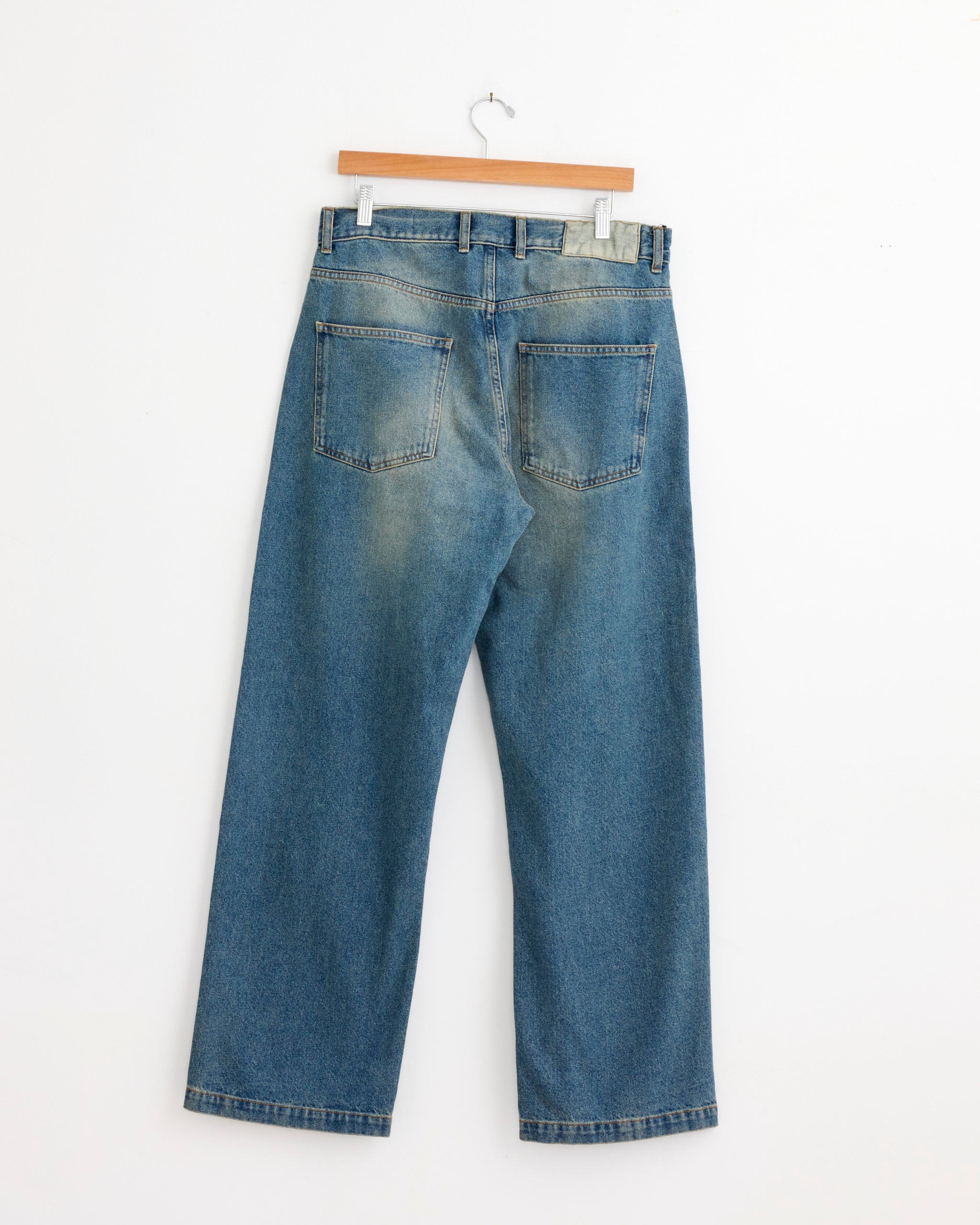 The mfpen Straight Cut Jean in Vintage Blue, crafted from organic cotton denim, is displayed from the back on a wooden hanger against a plain white background.
