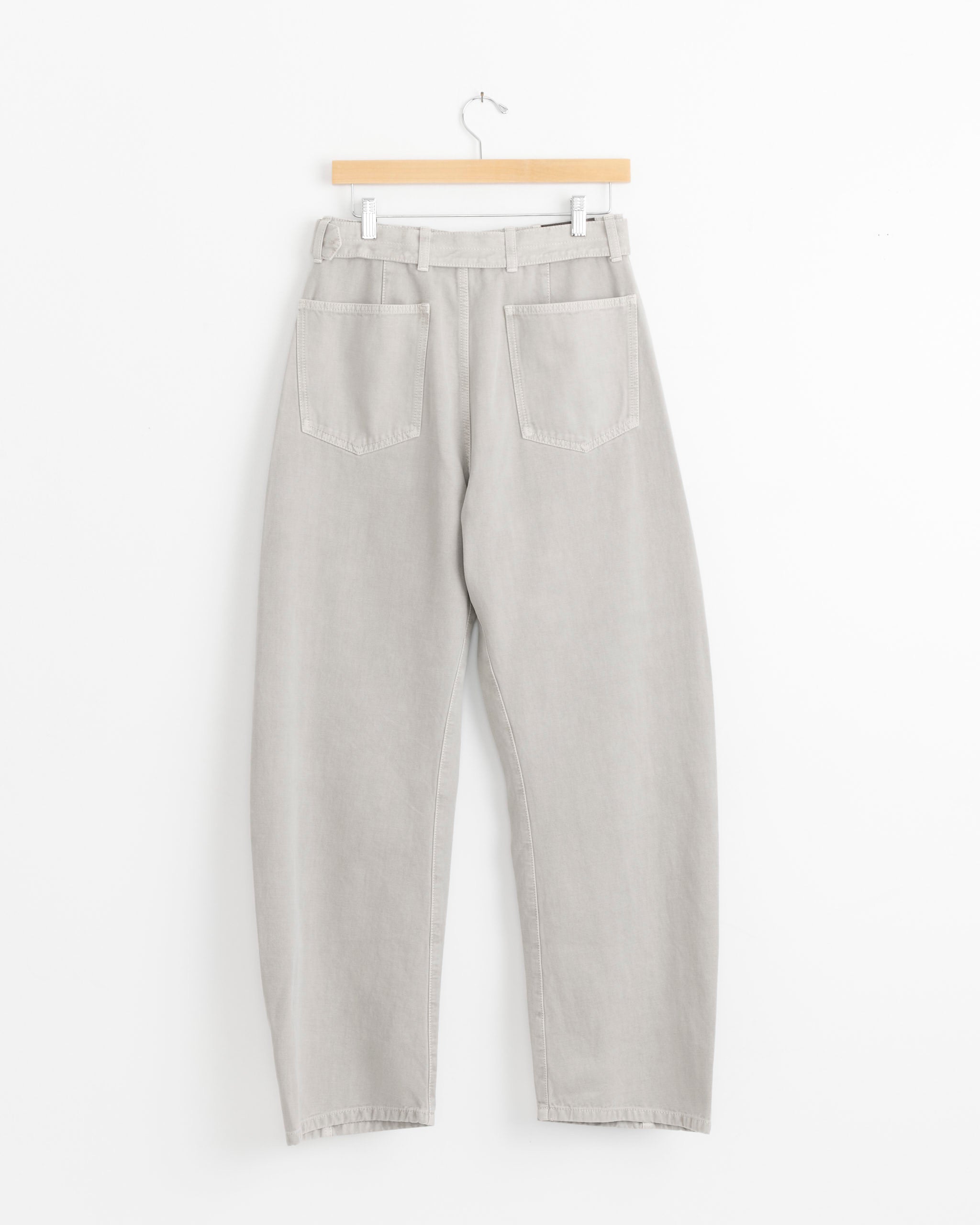 Lemaire Twisted Belted Pant in Moonstone with two large square back pockets, displayed on a wooden hanger against a plain white background.