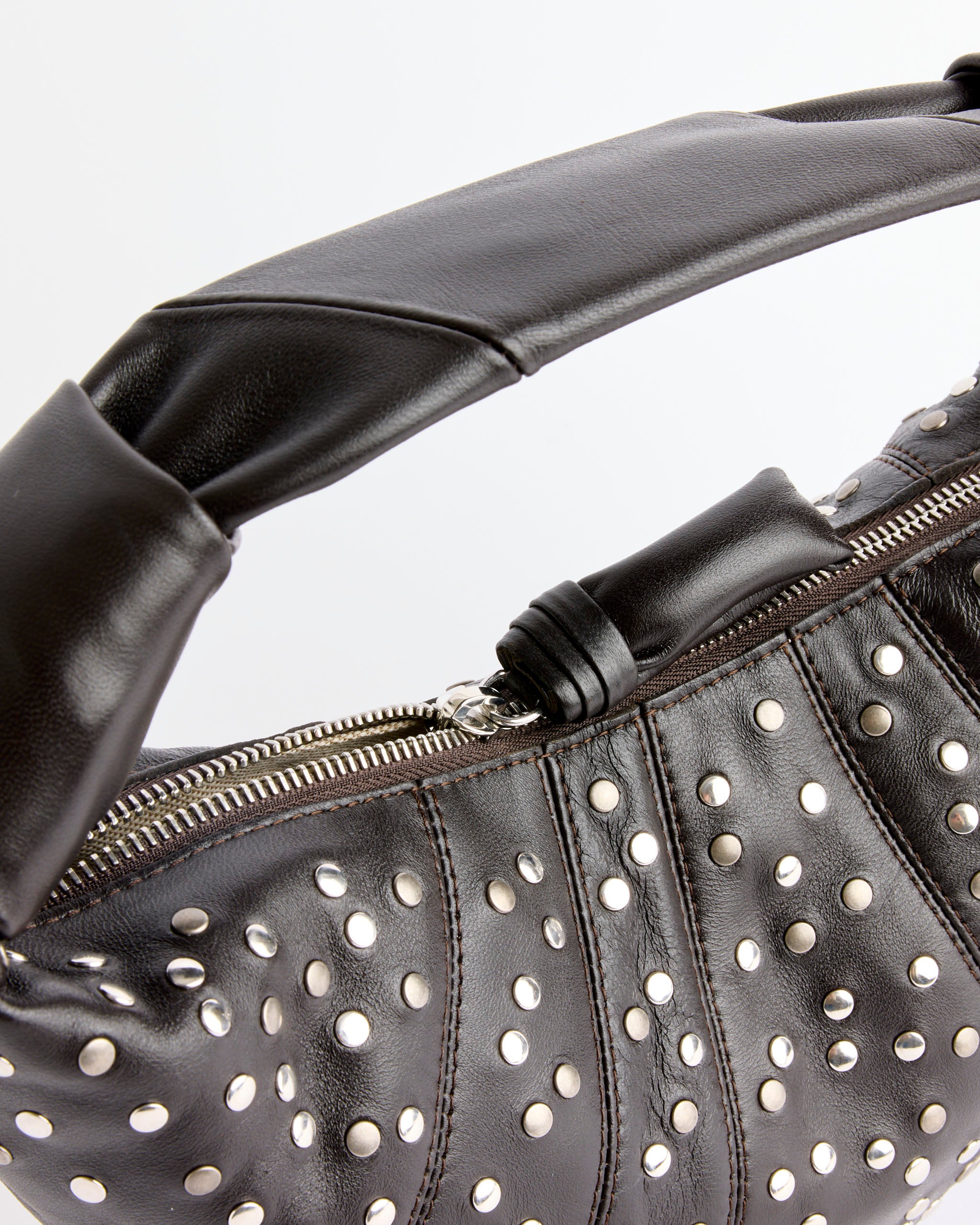 Close-up of Lemaire’s Mini Fortune Studs Croissant Bag in Dark Chocolate, a designer shoulder bag with silver studs, chunky padded handle, nappa leather texture, and a silver zipper.